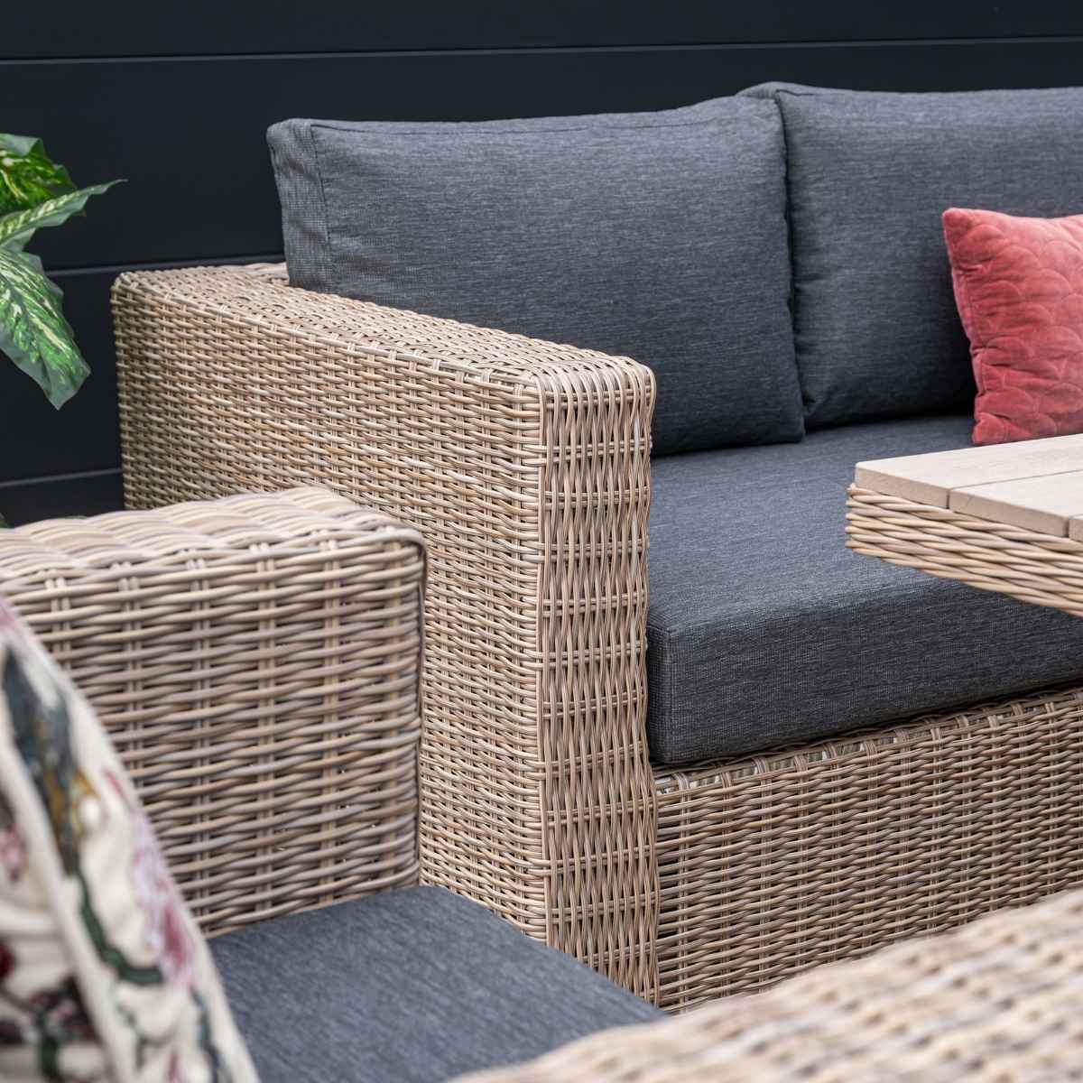 Gros plan d'un canapé en osier avec coussins gris et un coussin rouge. Fond sombre.