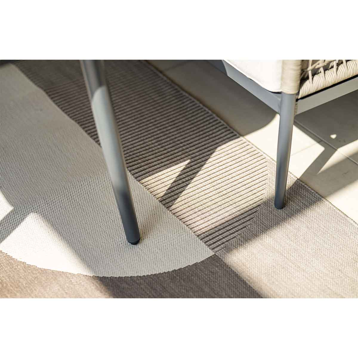Tapis à motif géométrique gris et blanc, pieds de table visibles.