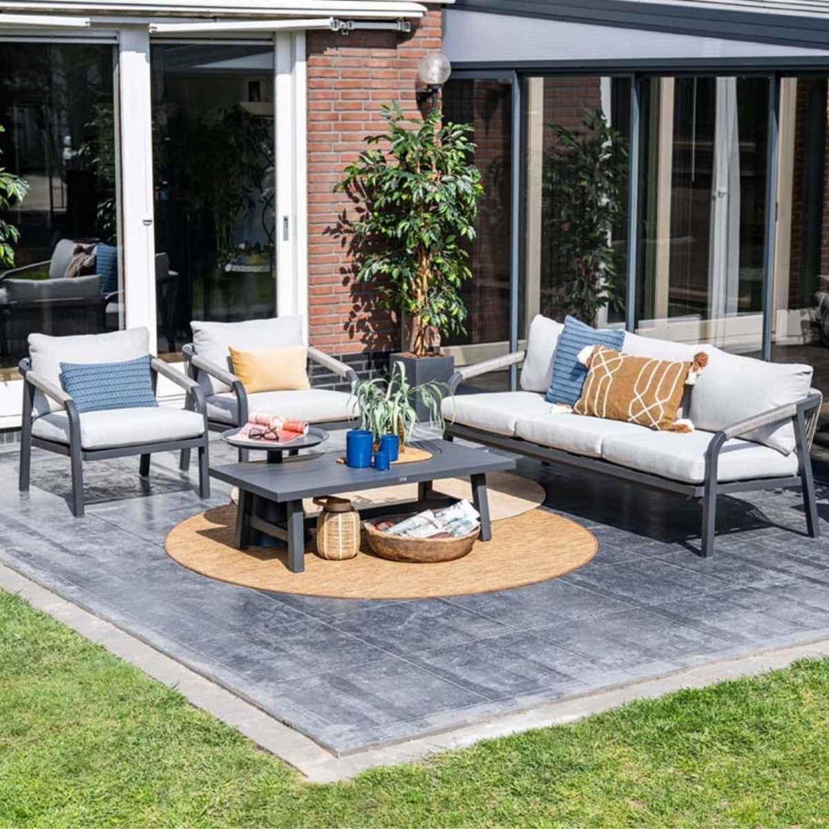 Outdoor patio set with a table, sofa, and chairs. Brick wall and greenery are visible.