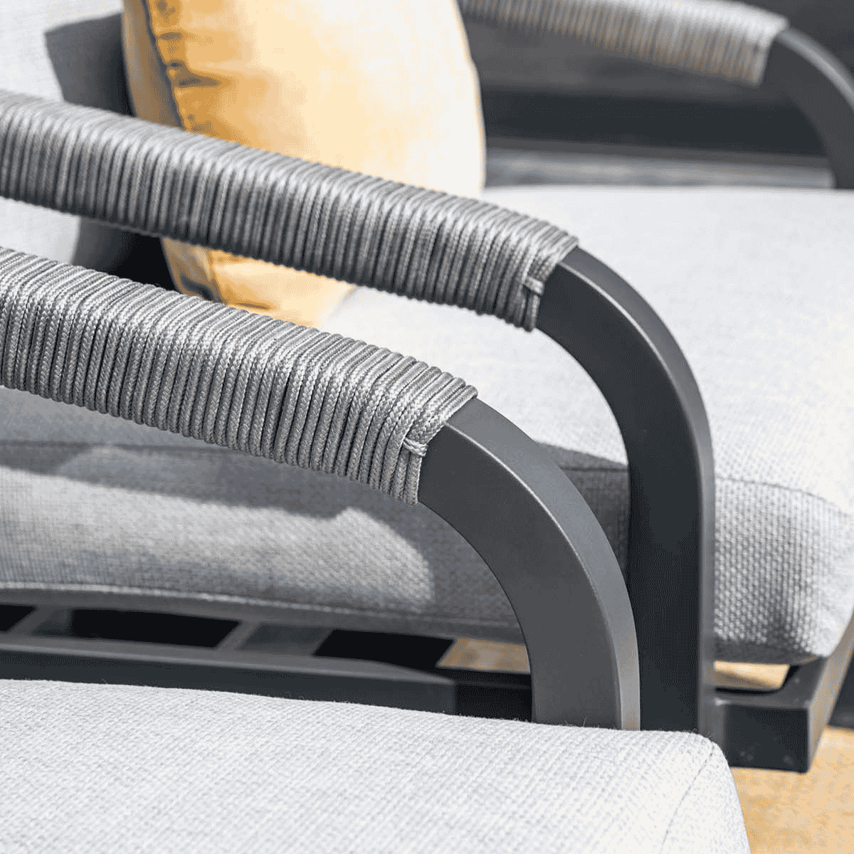 Close-up of gray armrests with rope detailing and a yellow pillow in the background.