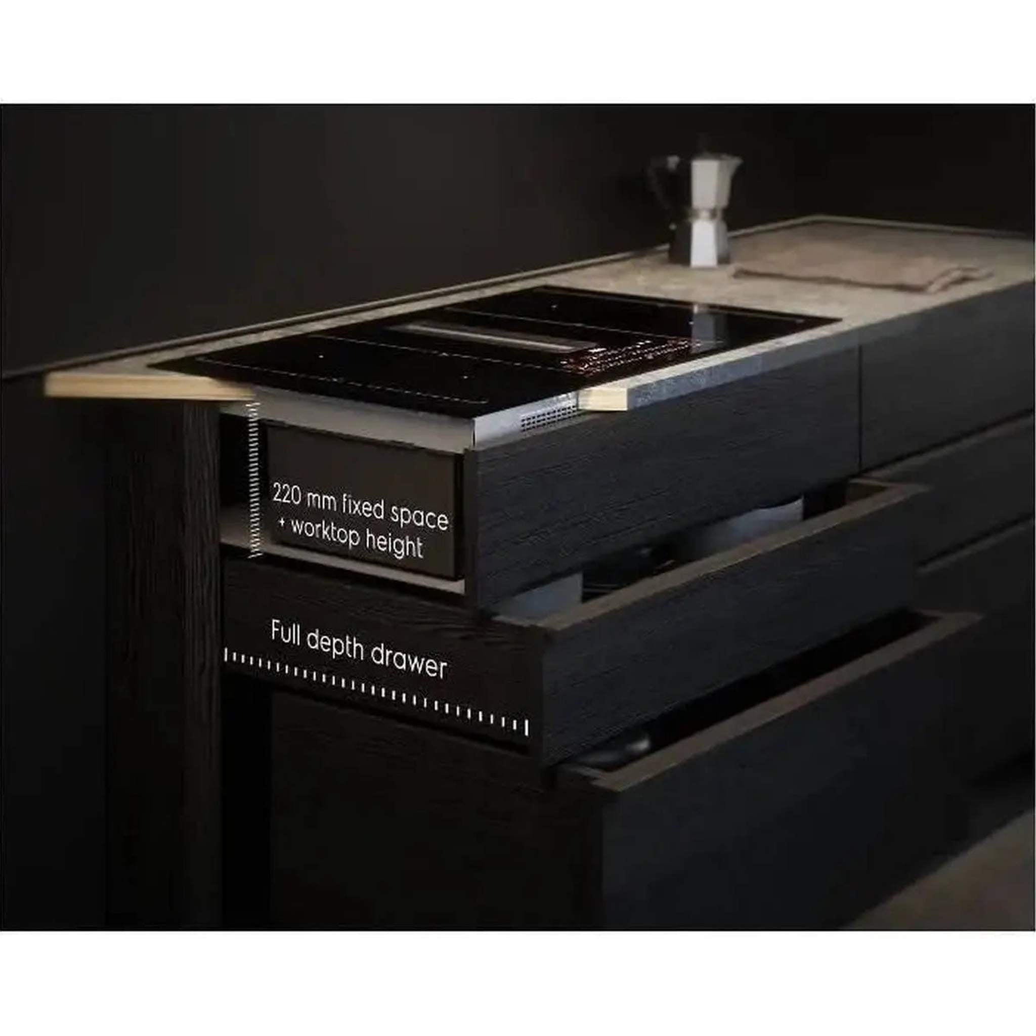 Czarna płyta grzewcza ze zintegrowanym wyciągiem. Szuflady poniżej, z etykietami. Kawiarka na górze.