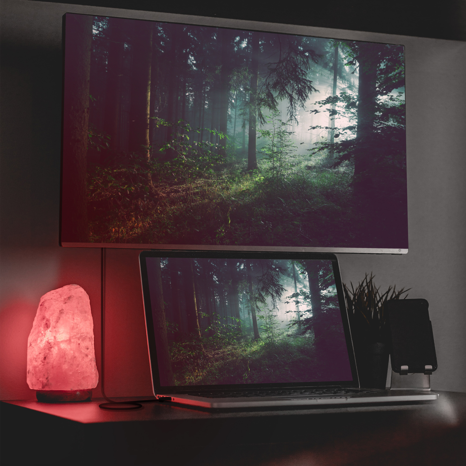 Escritorio con portátil, monitor y lámpara, mostrando una escena forestal.