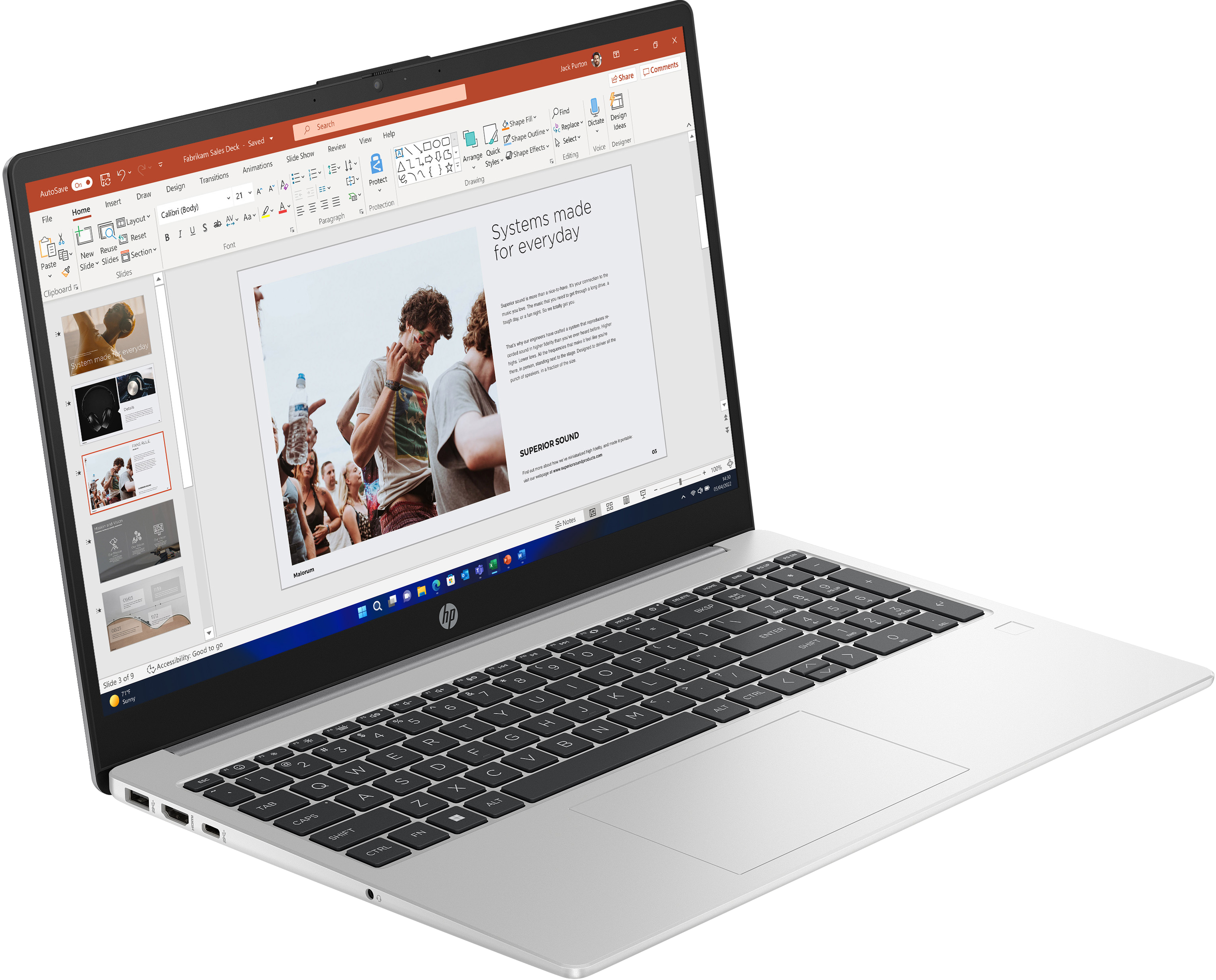 Ekran laptopa wyświetla prezentację programu PowerPoint. Klawiatura jest srebrna. Białe tło.