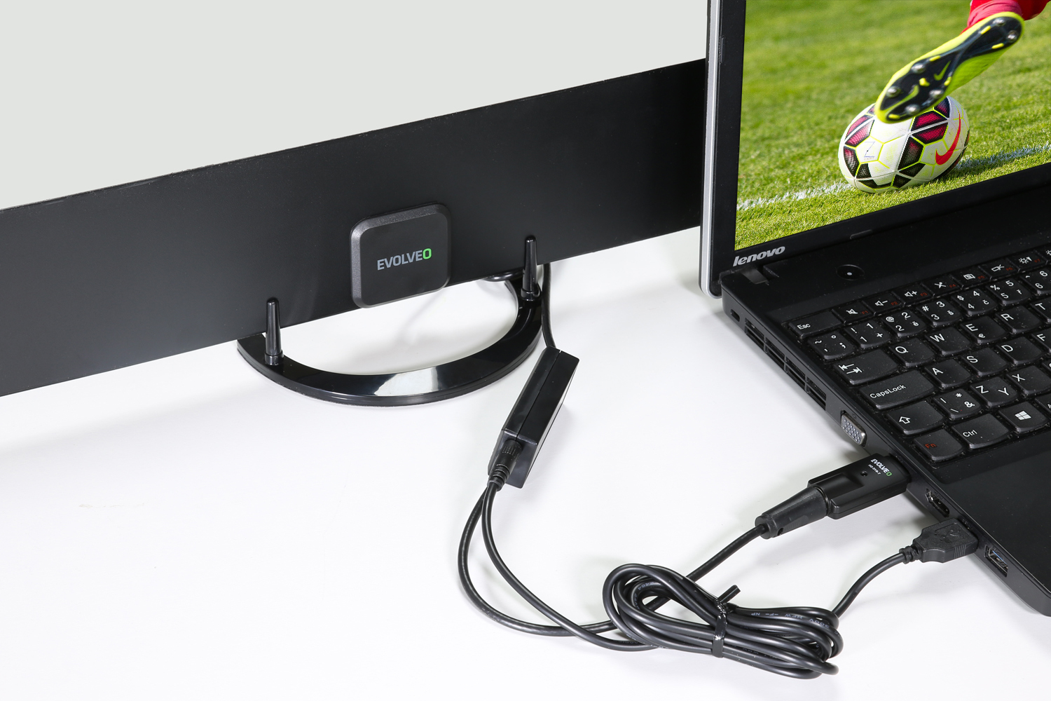Laptop podłączony do czarnej anteny. Ekran pokazuje mecz piłki nożnej. Kable są widoczne.