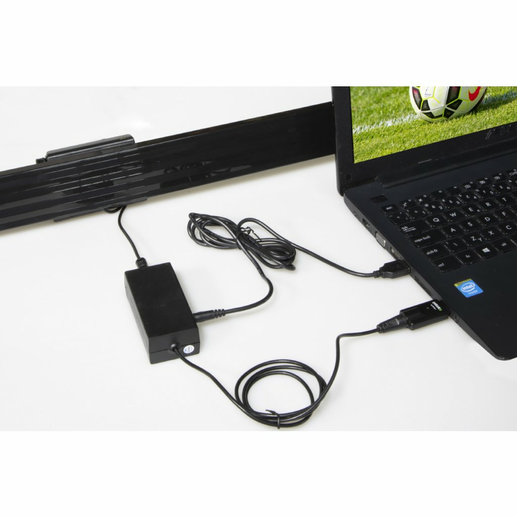 Laptop podłączony do czarnego zasilacza. Monitor pokazuje mecz piłki nożnej.