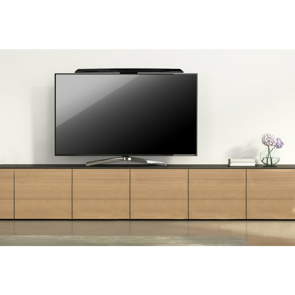 Salon z telewizorem na szafce. Soundbar nad TV. Wazon z kwiatami po prawej.