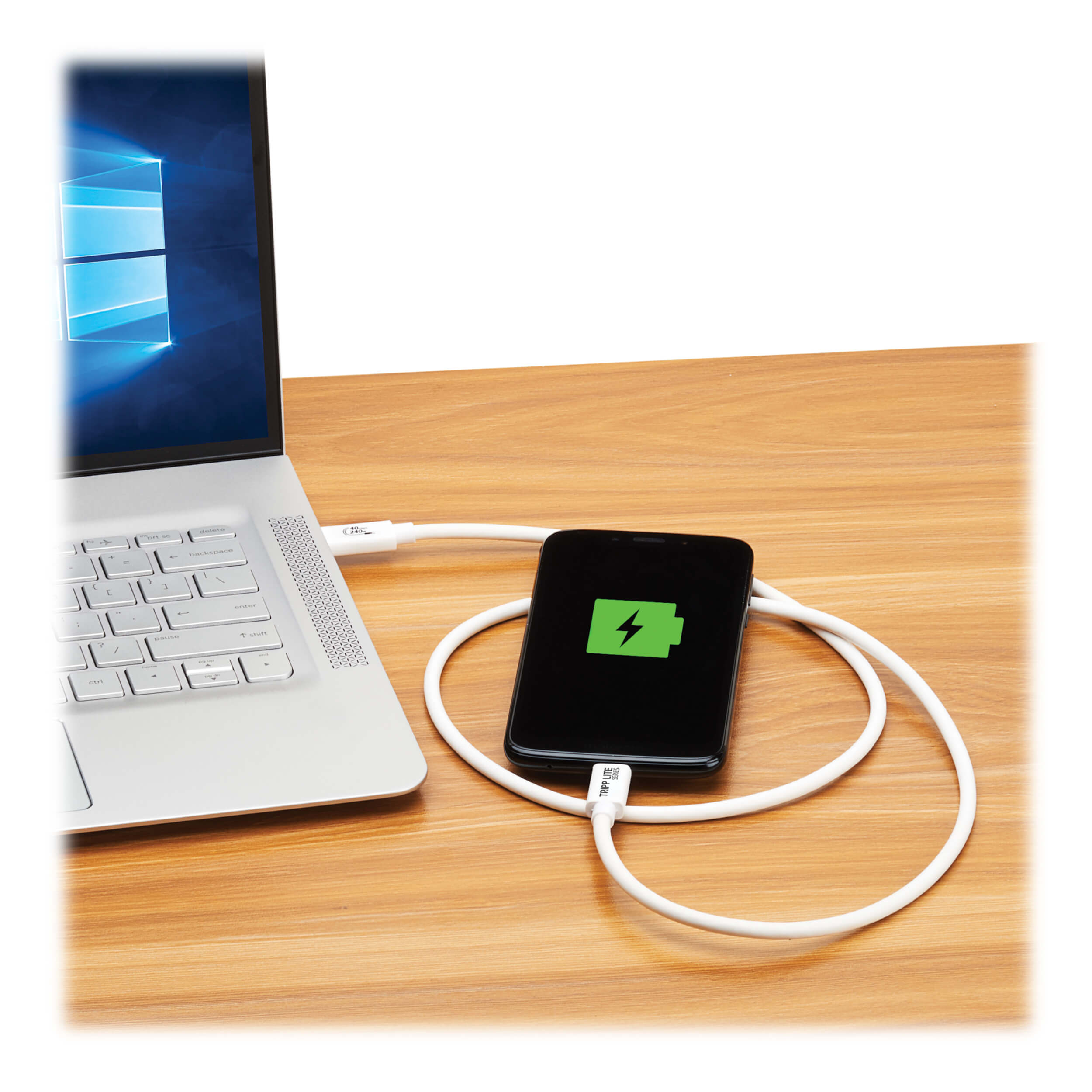 Laptop, telefon ładujący się za pomocą białego kabla USB-C. Telefon pokazuje ikonę ładowania. Drewniane tło.