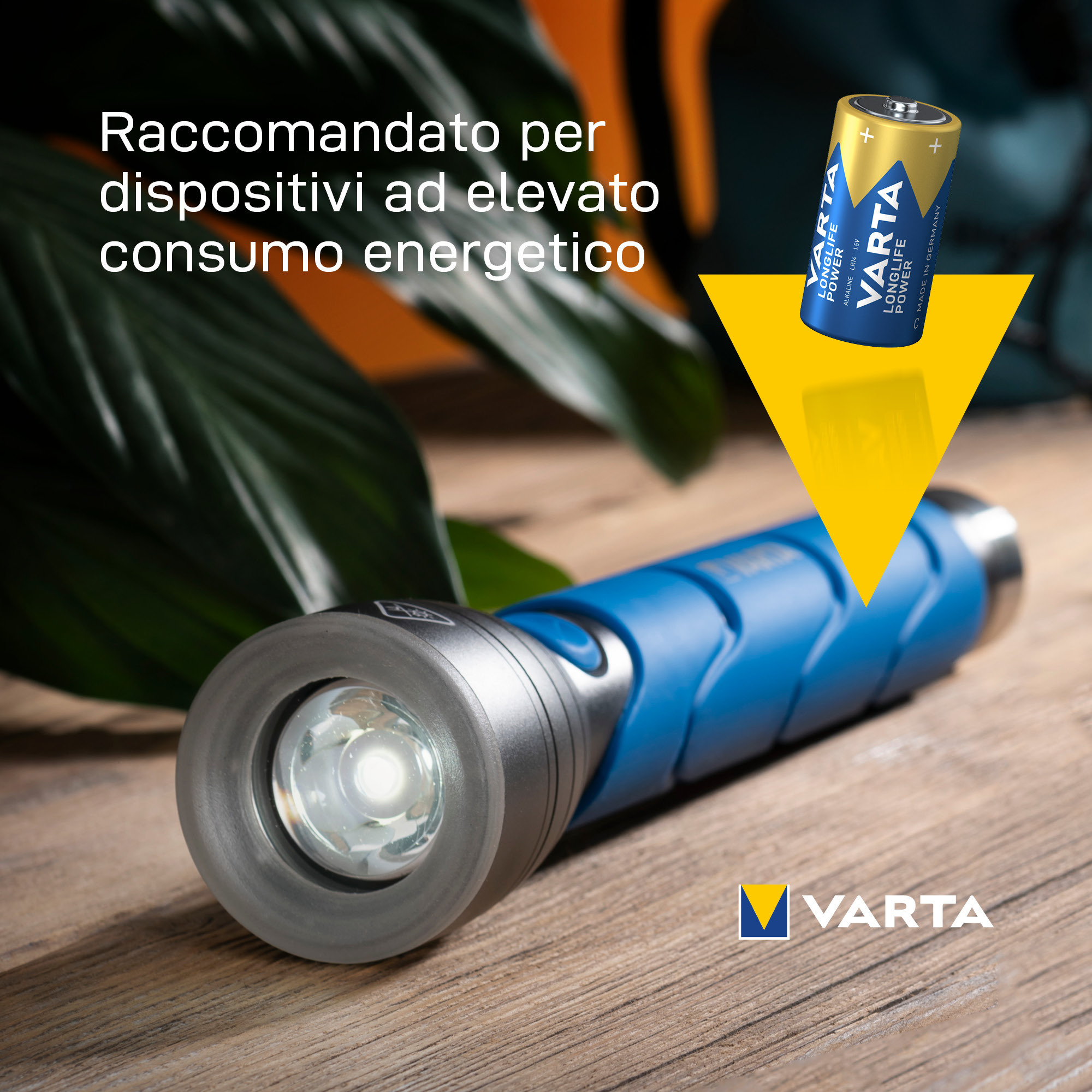 Una torcia blu e argento su una superficie di legno. Una batteria VARTA sullo sfondo.