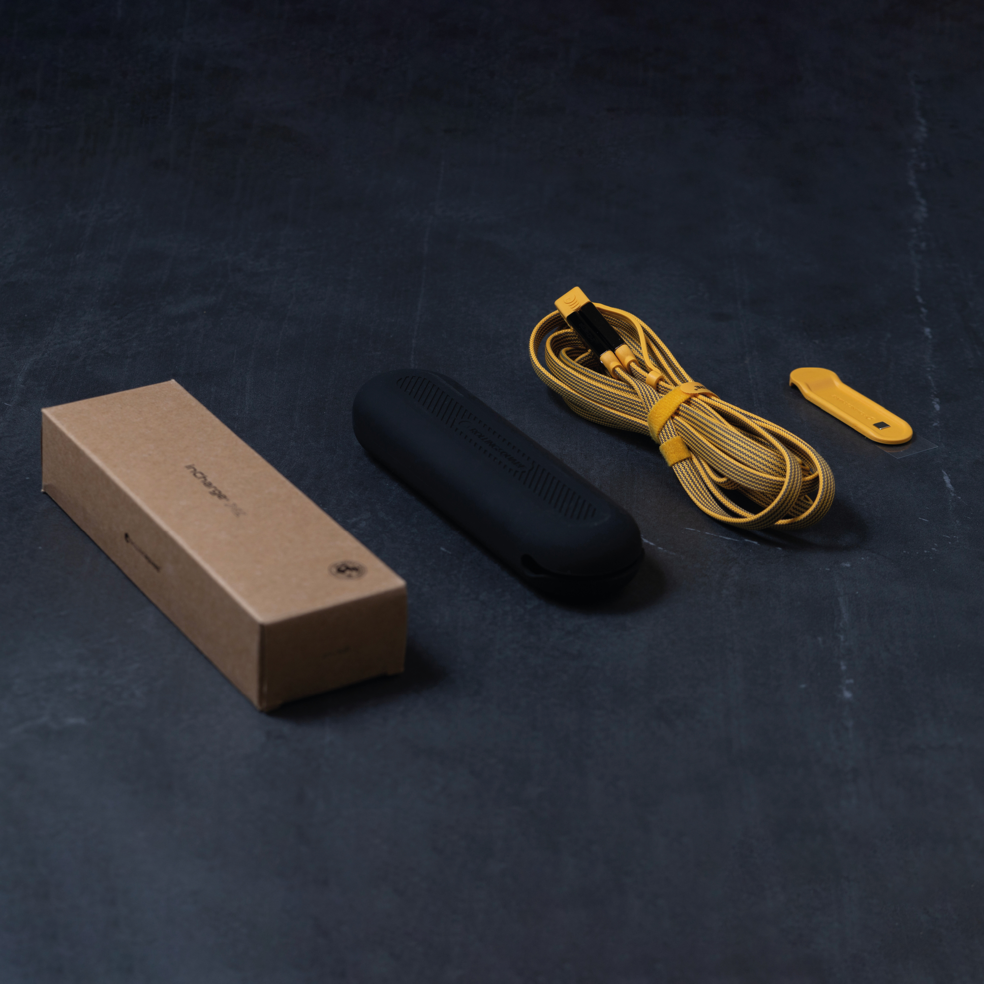 Eine Box, ein schwarzes Etui und ein gelbes Kabel auf dunkler Oberfläche.