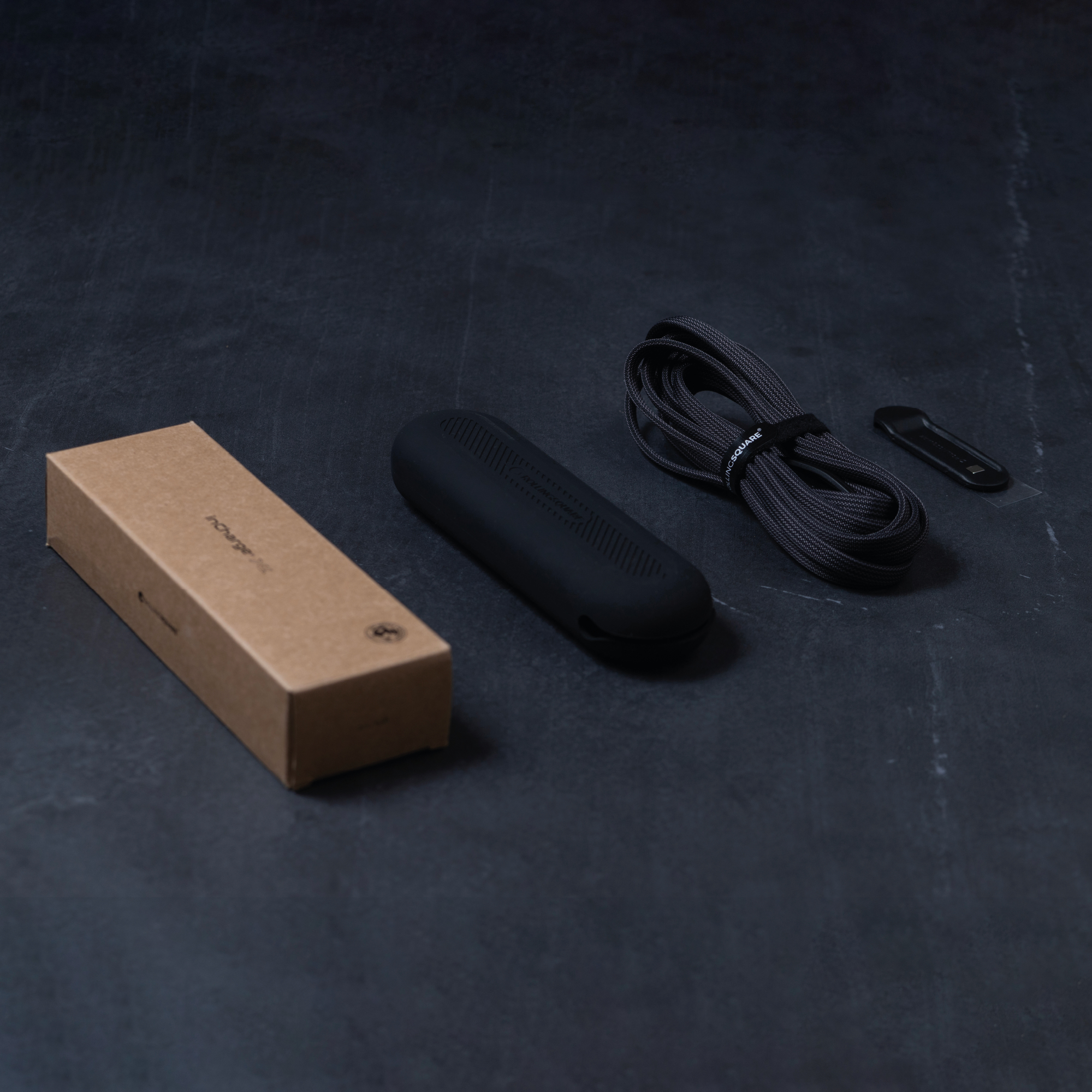 Eine Box, ein Kabel und ein schwarzes Gerät auf dunkler grauer Oberfläche.