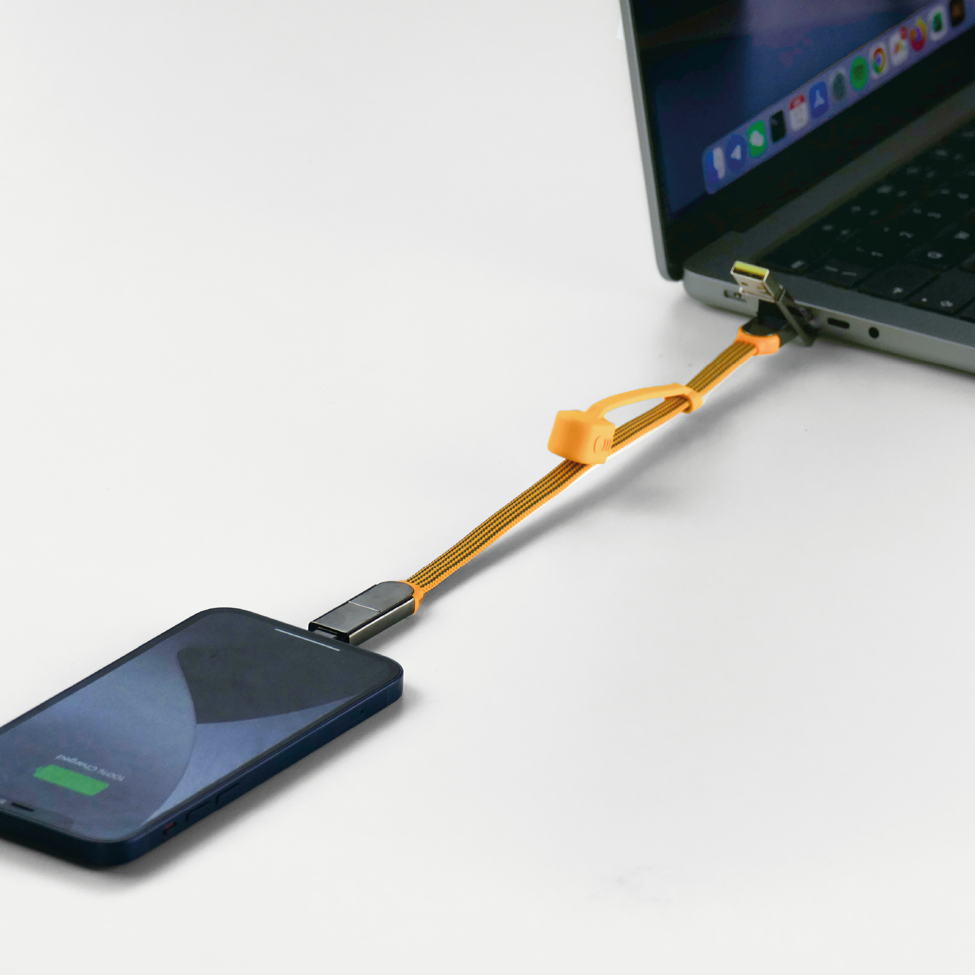 Telefon wird mit einem orangefarbenen geflochtenen Kabel an einem Laptop geladen.