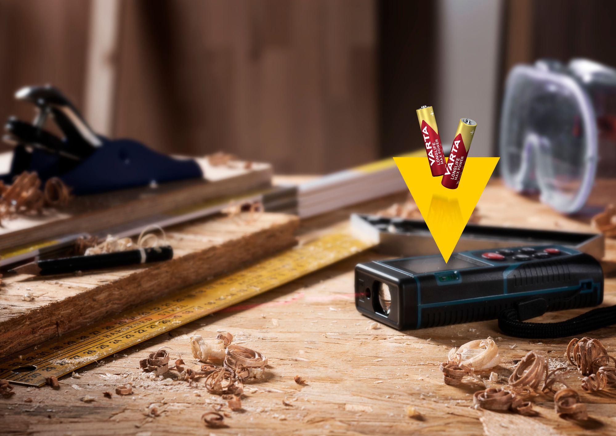 Laser distance meter and batteries on a wooden surface with wood shavings.