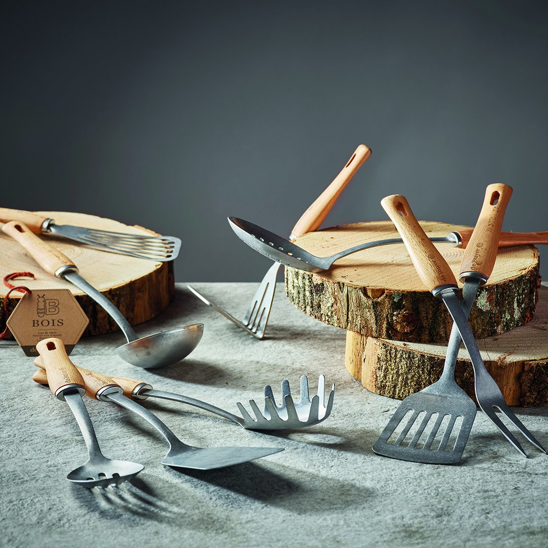 Vari utensili da cucina con manico in legno su blocchi di legno e una superficie di pietra.