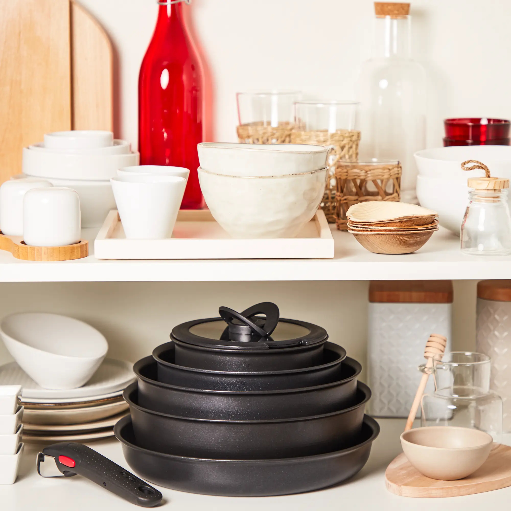 Białe półki wypełnione naczyniami kuchennymi: miskami, patelniami, butelkami, deskami do krojenia i innymi akcesoriami.