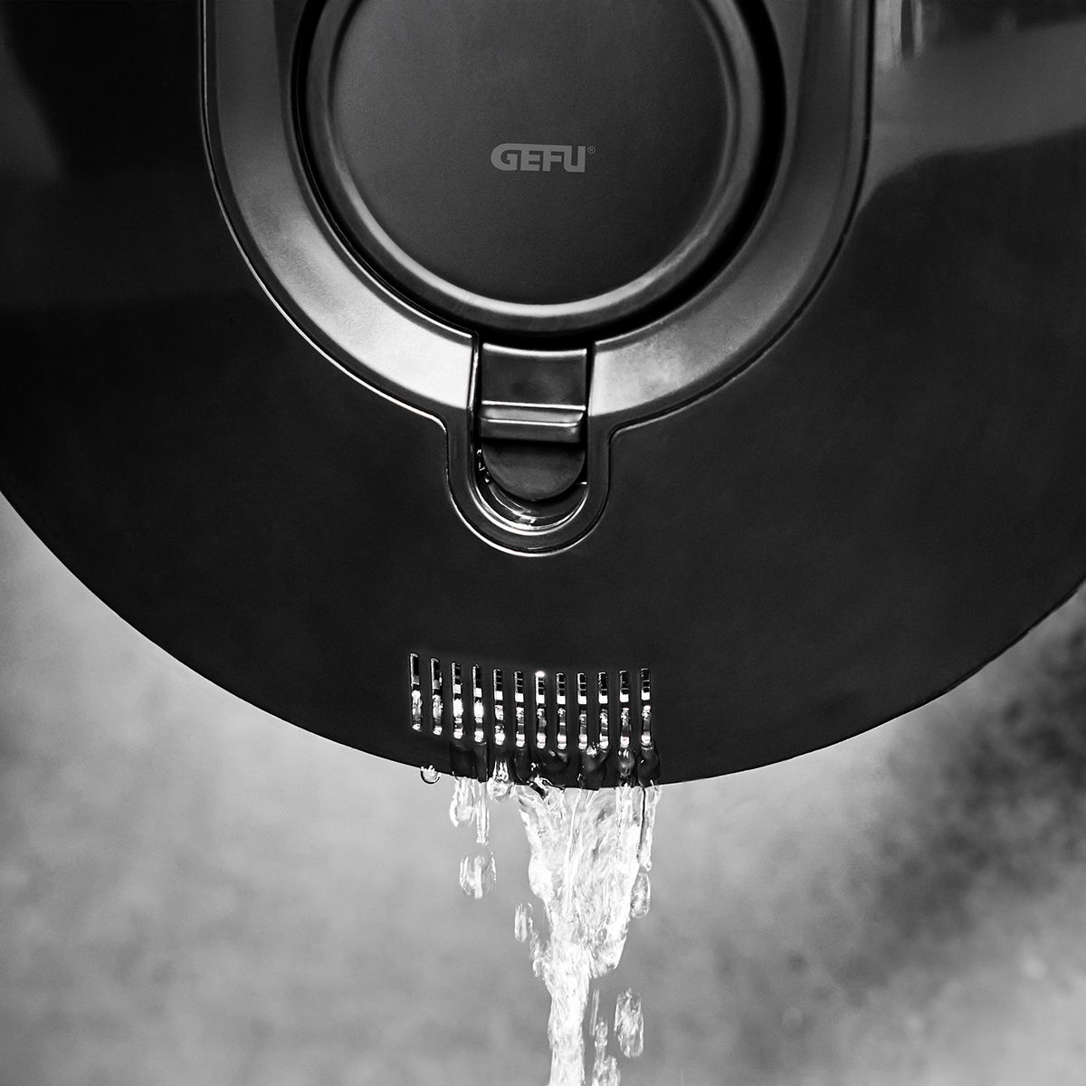 Woda wylewająca się z czarnego urządzenia kuchennego. Urządzenie jest czarne i ma logo. Białe tło.