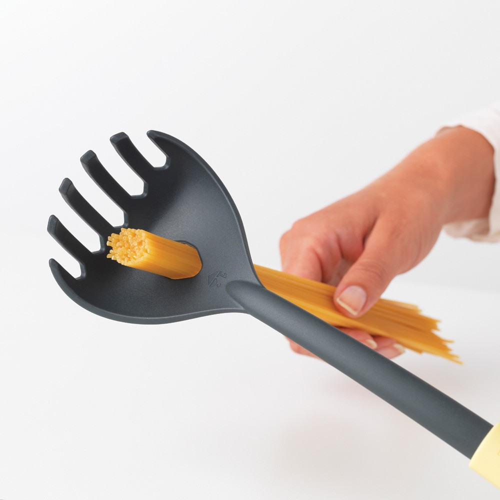 Eine Pastagabel hält Pasta. Ein Bündel Pasta liegt daneben. Weißer Hintergrund.