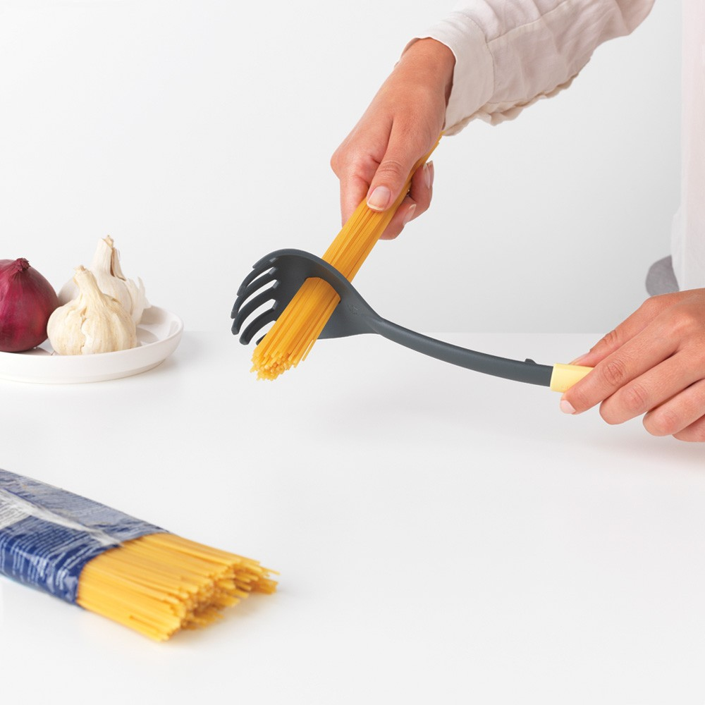 Hände halten Spaghetti mit einer Spaghetti-Gabel neben einer Packung und Zutaten.