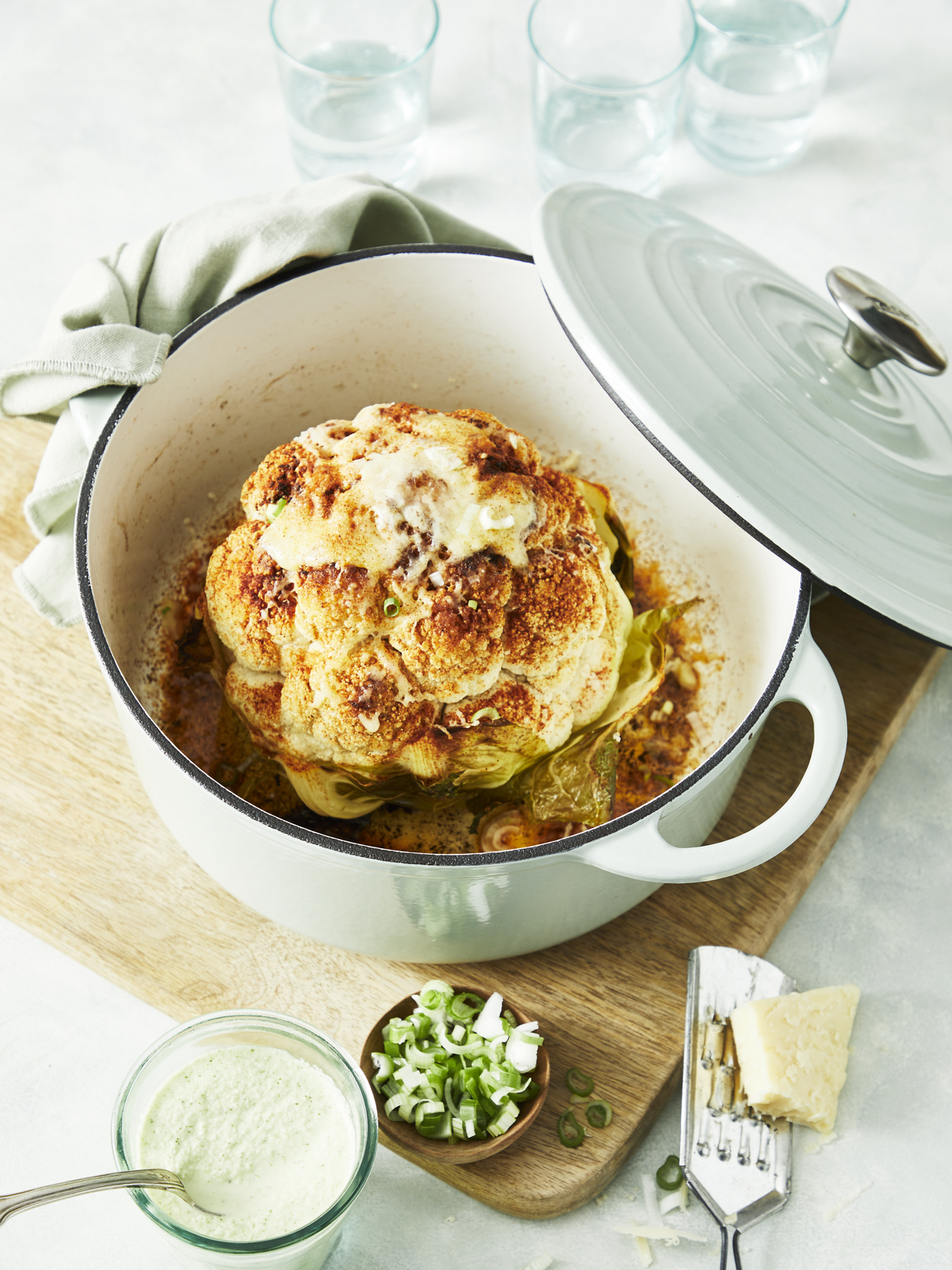 Pieczony kalafior w garnku z serem. Zielone zioła, sos i składniki na drewnianej desce.