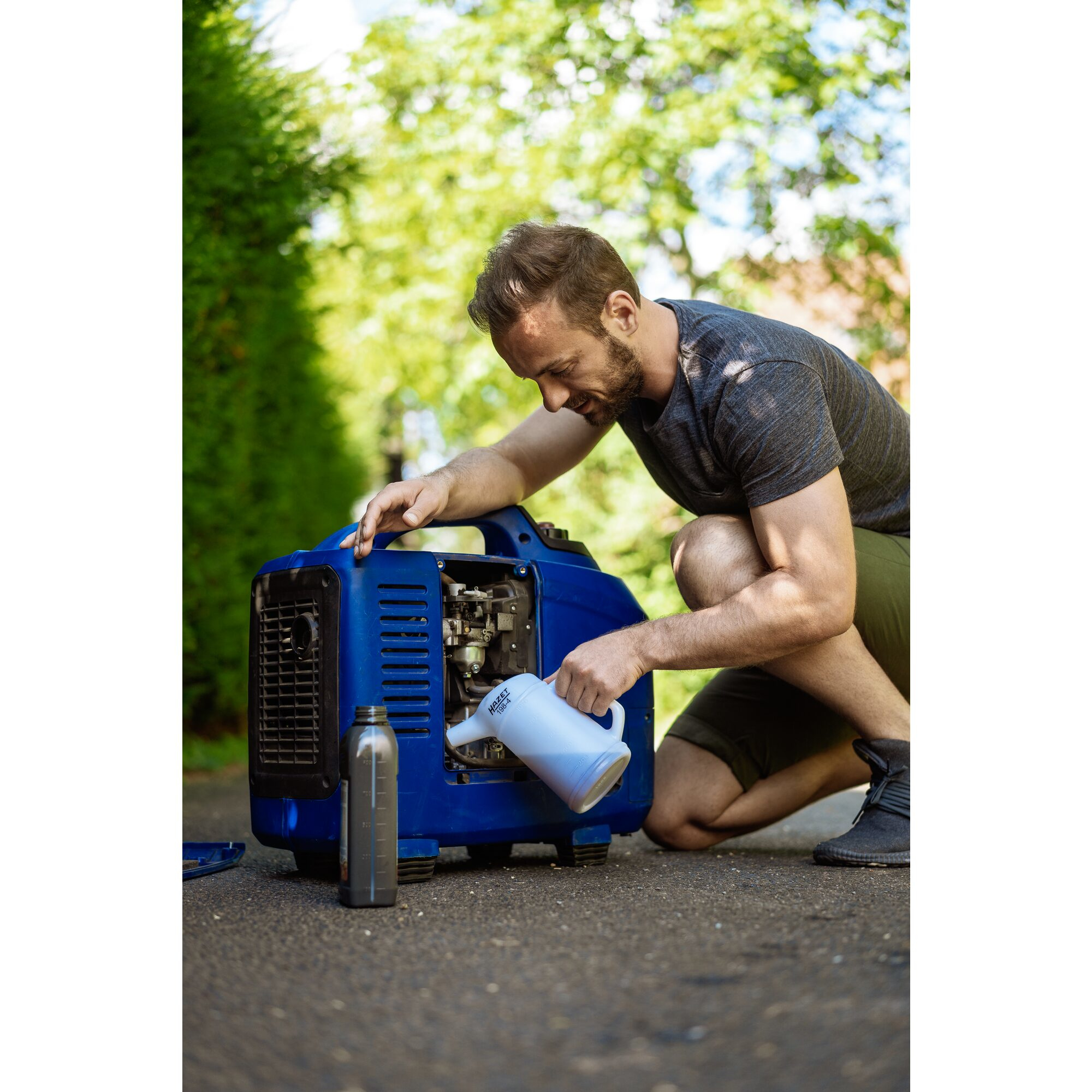Mann befüllt einen blauen Generator mit Öl, im Freien.