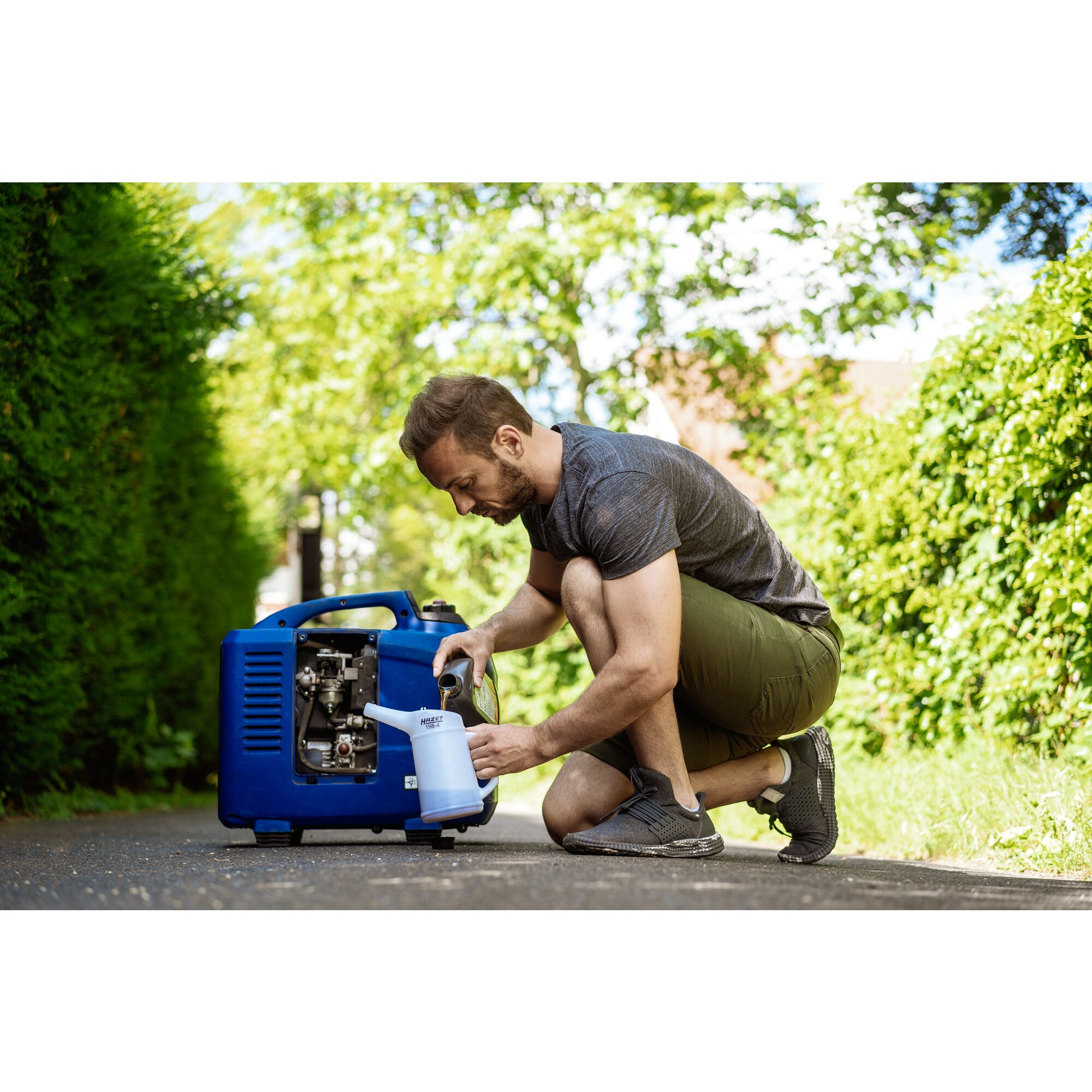 Ein Mann kniet und gießt Öl aus einem weißen HAZE 198-4 Behälter in einen blauen Generator. Grüner Hintergrund.