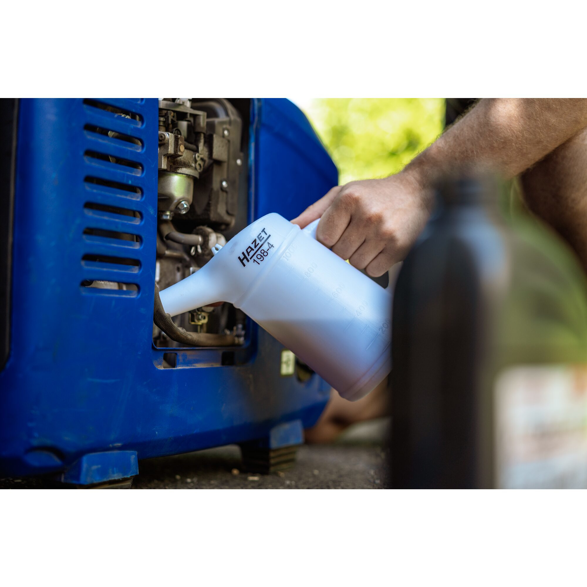 Eine Person gießt Flüssigkeit aus einem weißen HAZE 198-4 Behälter in eine blaue Maschine. Der Hintergrund ist unscharf.