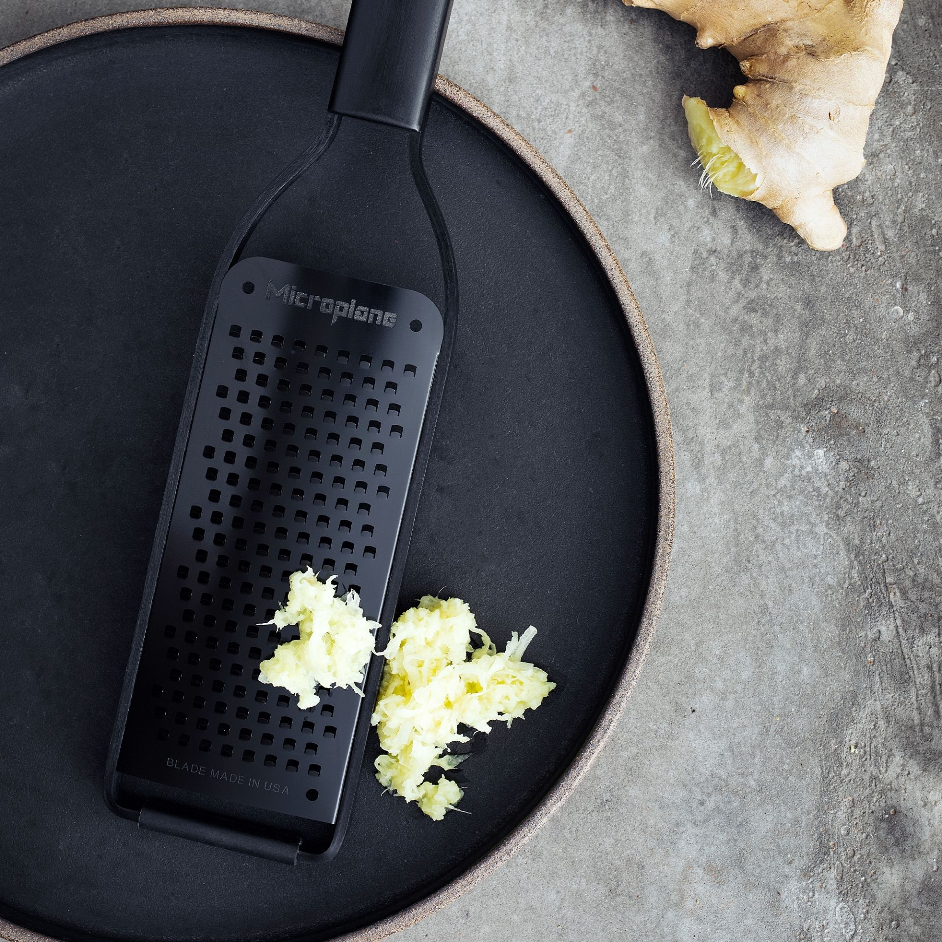 Czarna tarką z startym imbirem na czarnym talerzu na szarej powierzchni.