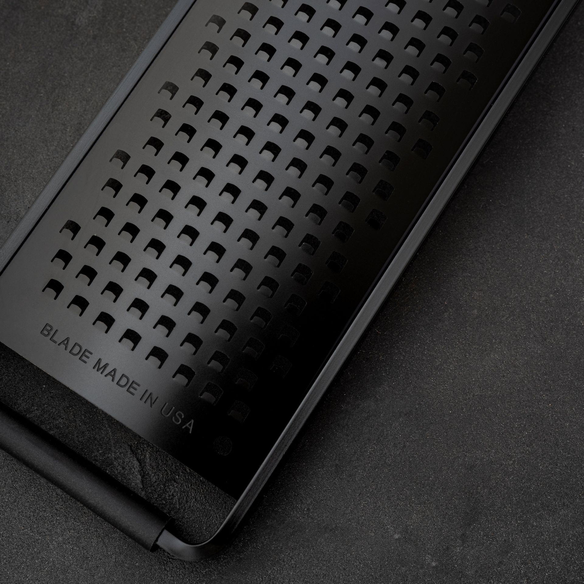 Czarna tarka z wieloma otworami i napisem 'BLADE MADE IN USA' na ciemnej powierzchni.