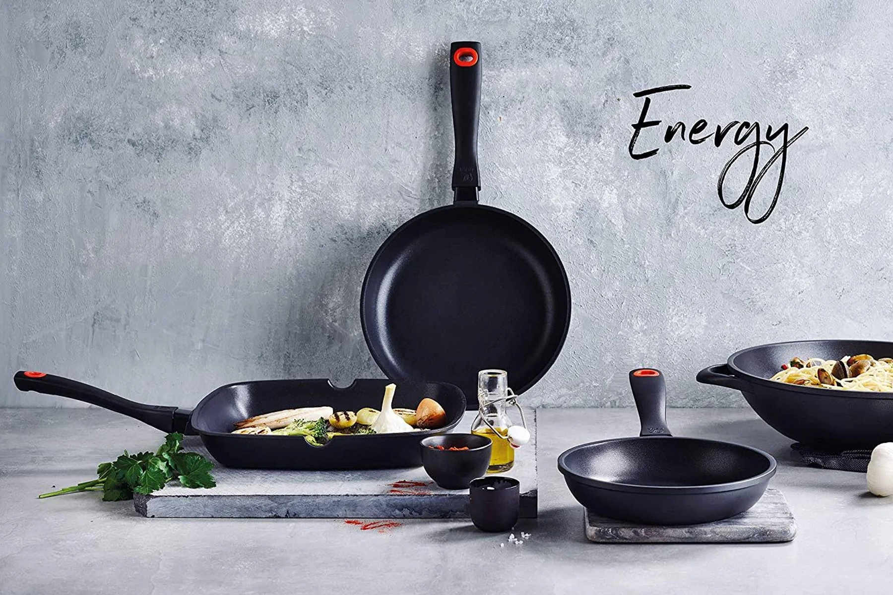 Sammlung schwarzer Pfannen mit Essen und Öl auf grauer und weißer Oberfläche. Energy Text.
