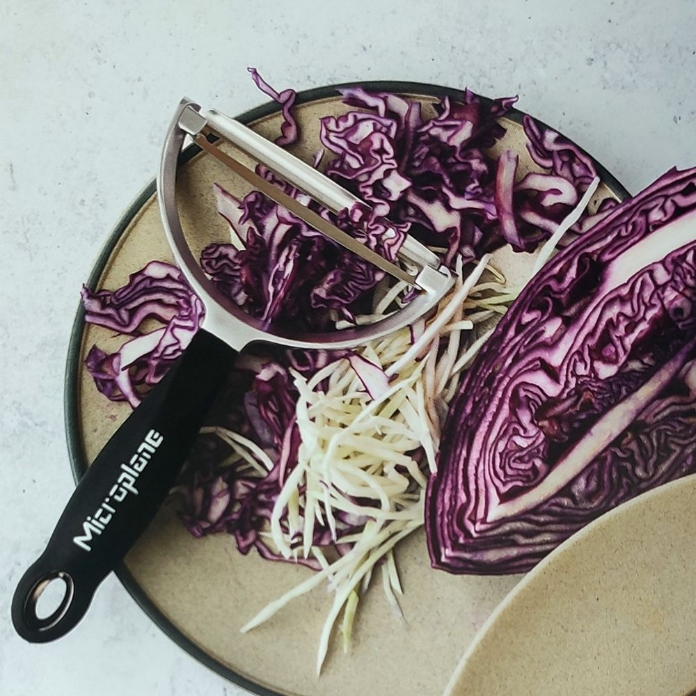 Ein Schäler mit Rotkohl und weißem, geschnittenem Gemüse auf einem Teller.