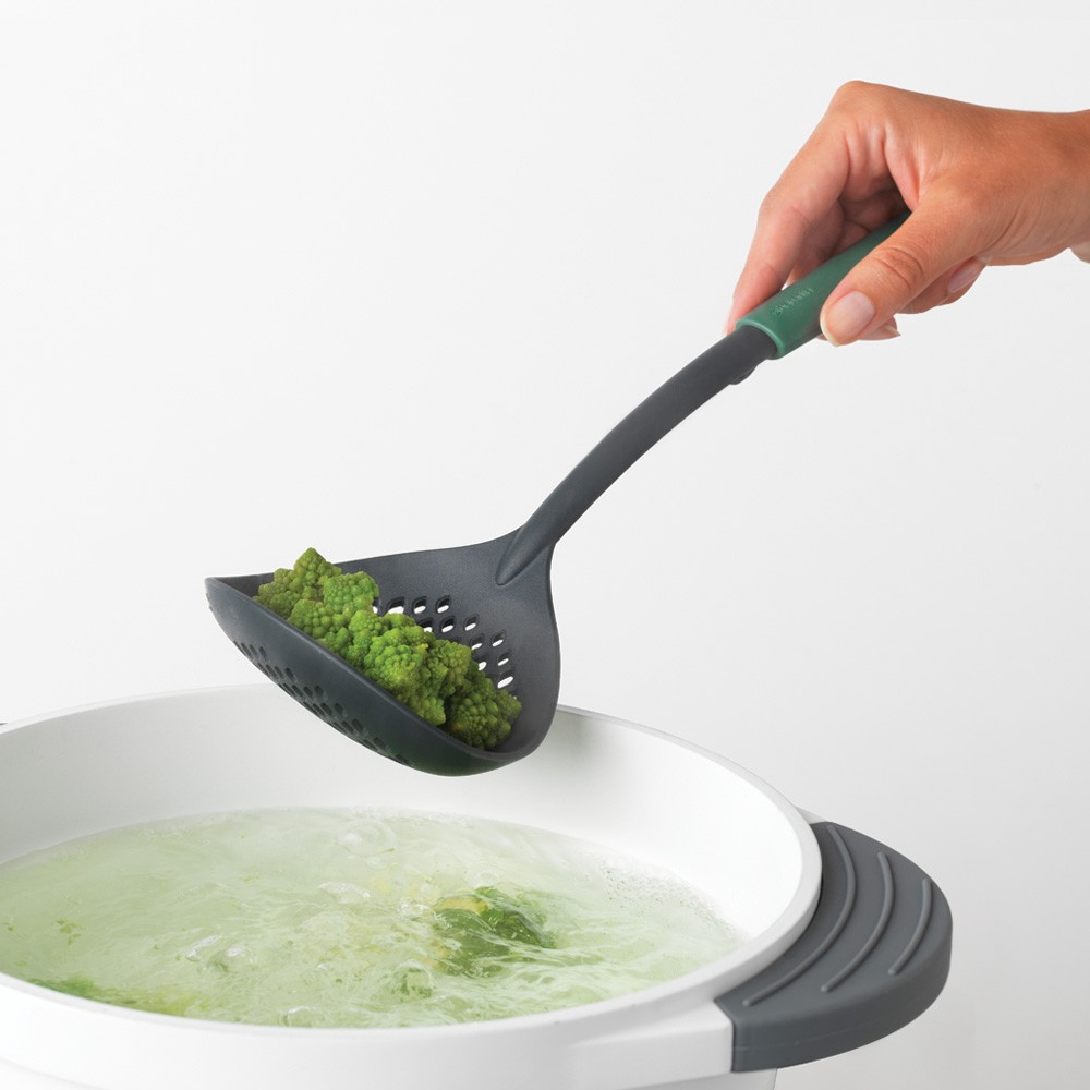 Una mano che tiene una schiumarola verde sopra una pentola di acqua bollente.