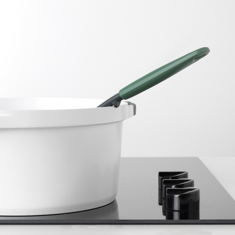 Pentola bianca su piano cottura nero con utensile con manico verde.