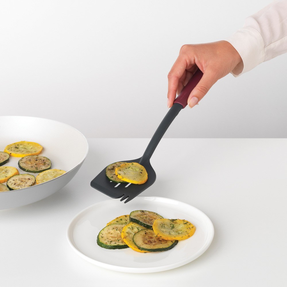 Persona usa spatola per mettere fette di zucchine su un piatto. Ciotola di fette di zucchine vicina.