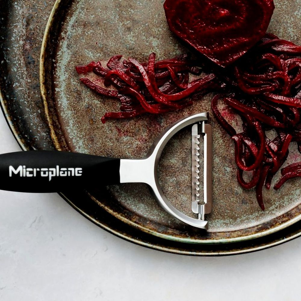 Microplane-Schäler und geschnittene Rüben auf einem Teller. Weißer Hintergrund.