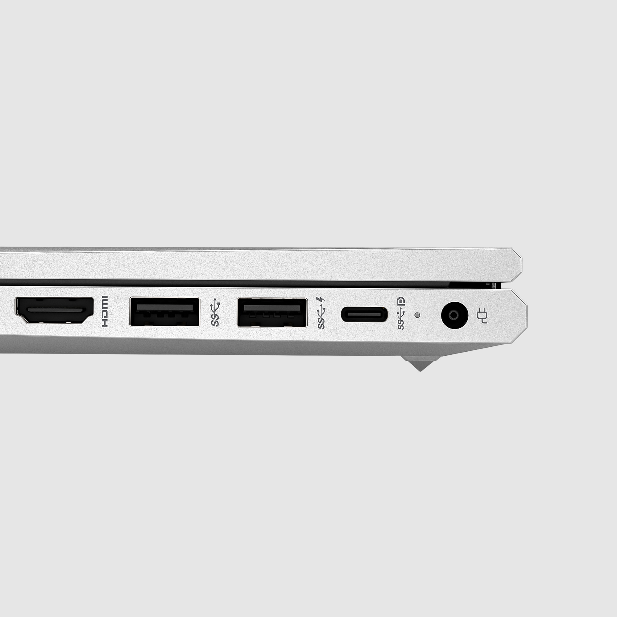 Vista laterale di un laptop argentato, porte visibili: HDMI, USB, USB-C e alimentazione. Sfondo grigio.