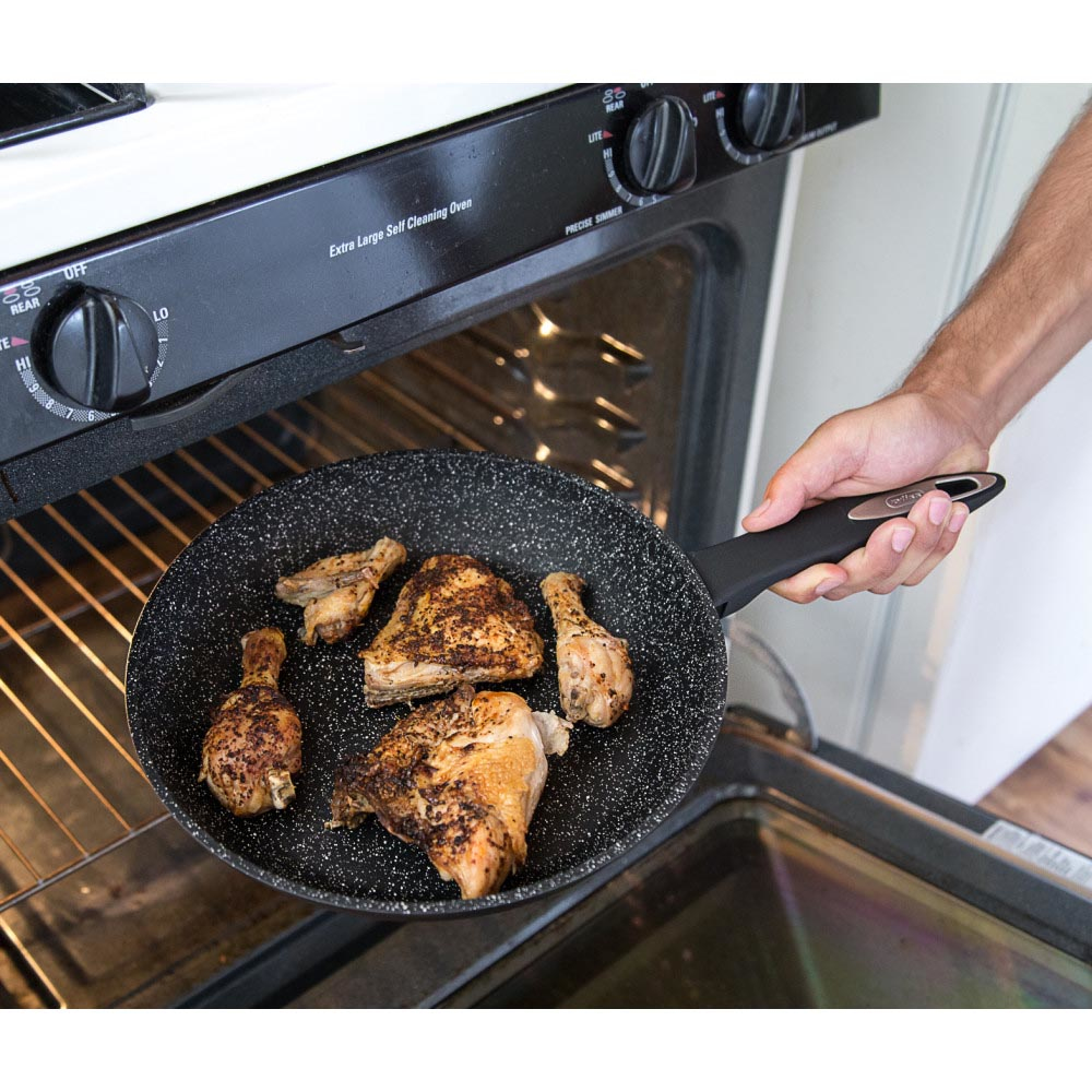 Ręka trzymająca patelnię z kawałkami gotowanego kurczaka nad piekarnikiem.