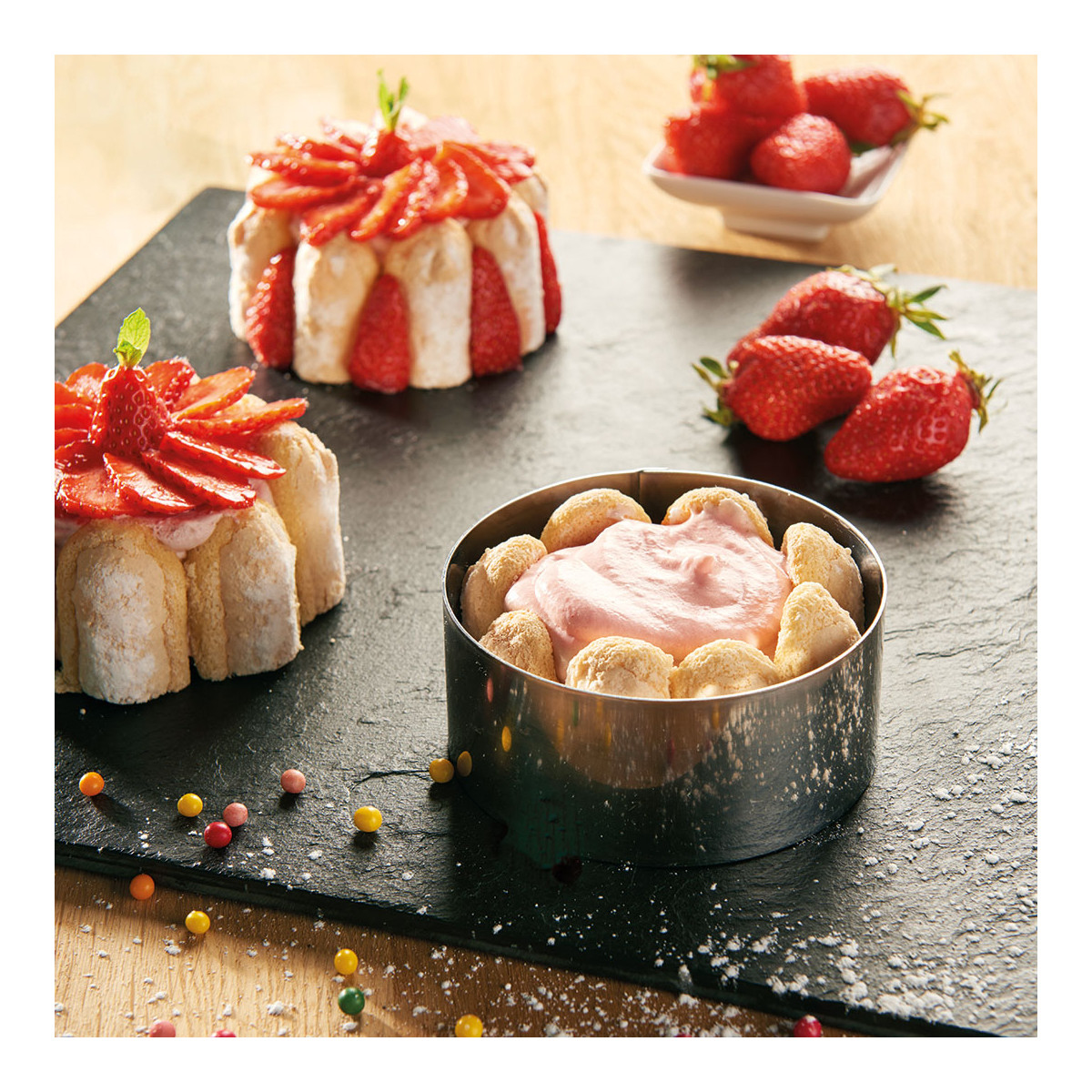 Erdbeerdesserts in Kuchenringen. Erdbeeren und bunte Süßigkeiten auf schwarzer Oberfläche.