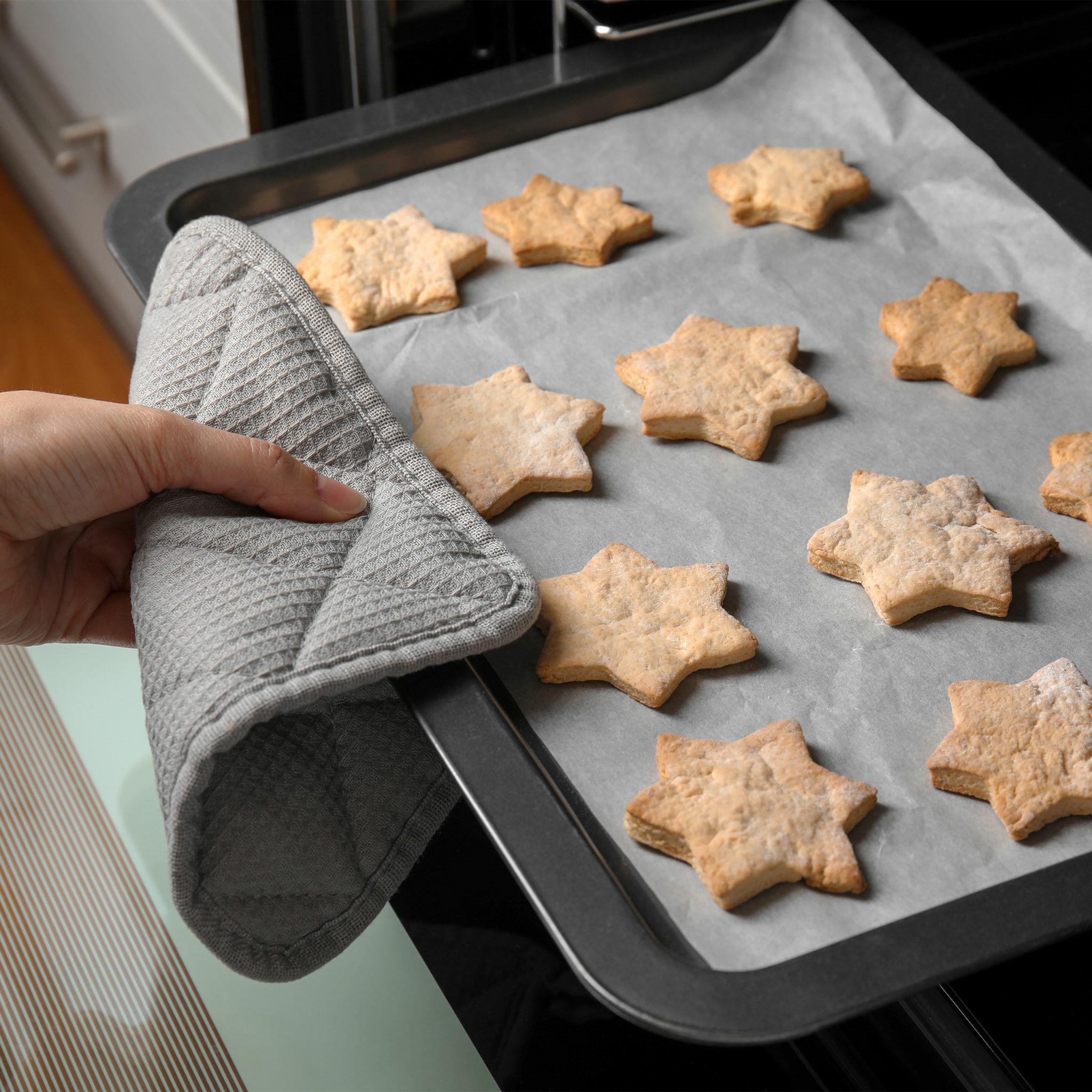 Sternförmige Kekse auf einem Backblech, gehalten von einem grauen Ofenhandschuh.