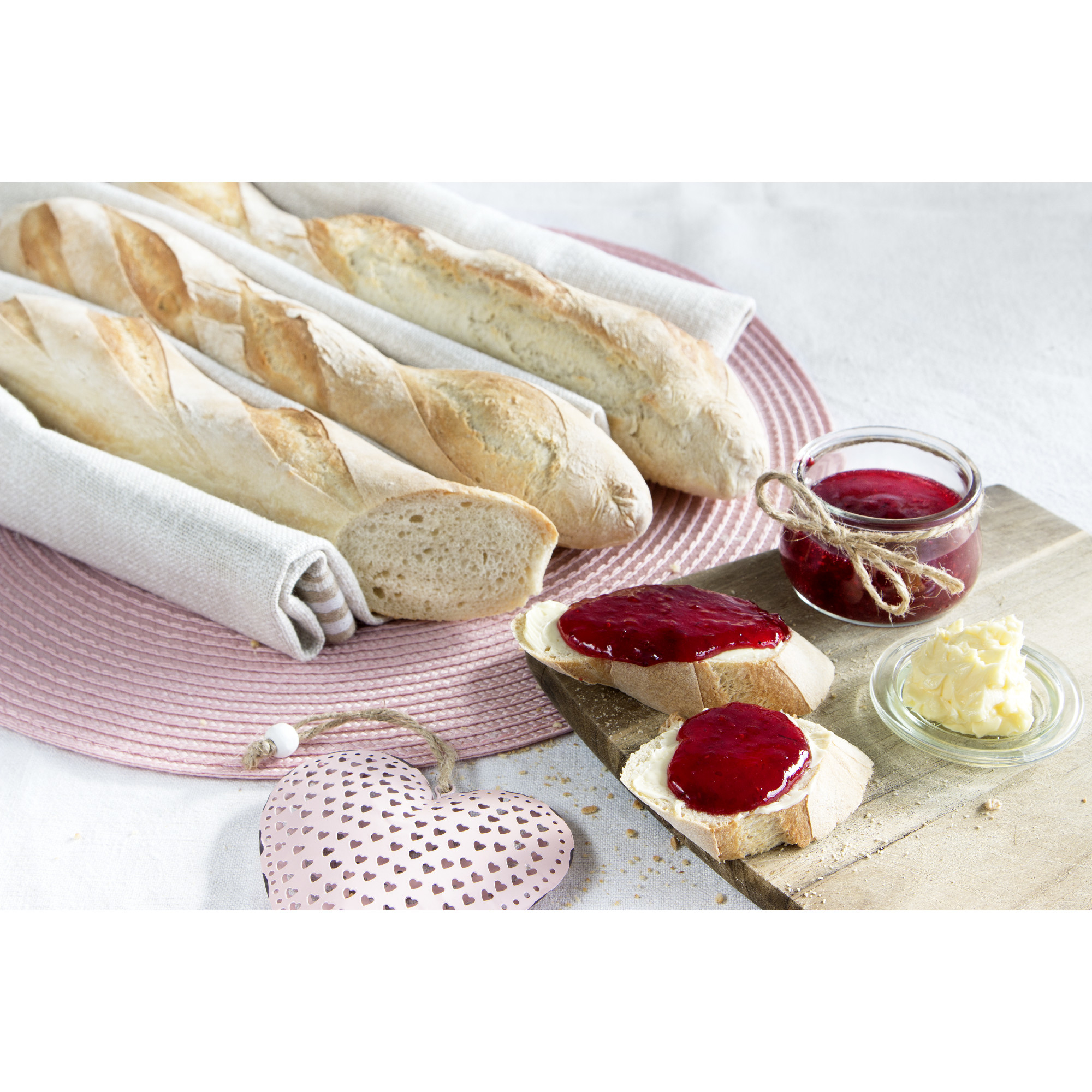 Baguettes, Brotscheiben mit Marmelade und Butter, Marmeladenglas, rosa Teller, Holzbrett.