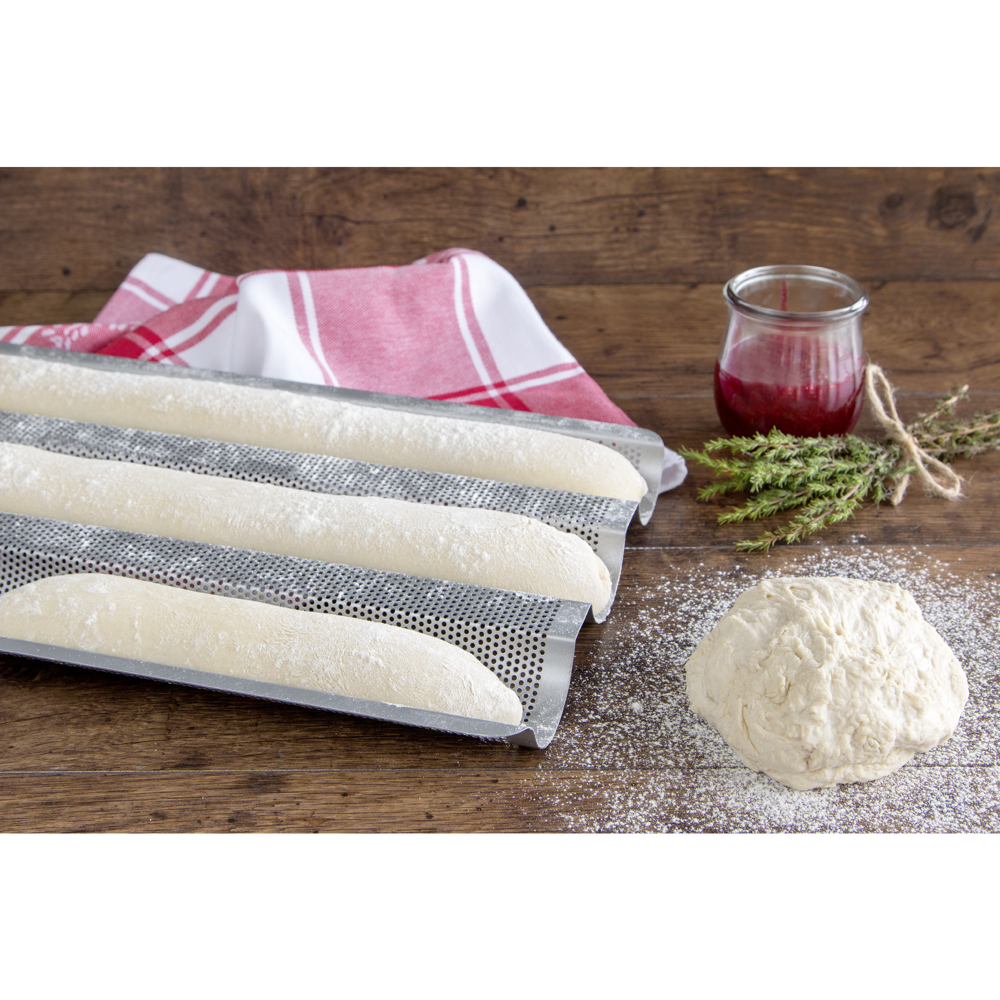Baguettes im Backblech, Teigkugel, Marmelade, Tuch und Thymian auf einem Holztisch.