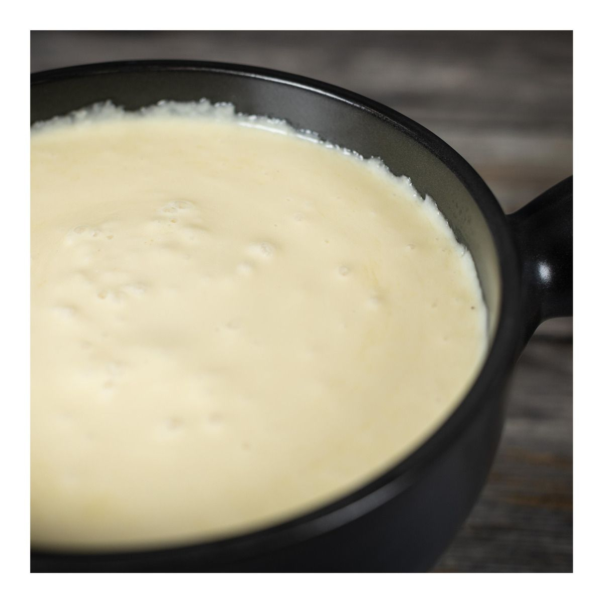 Czarny garnek z kremowym żółtym fondue, zbliżenie na drewnianej powierzchni.