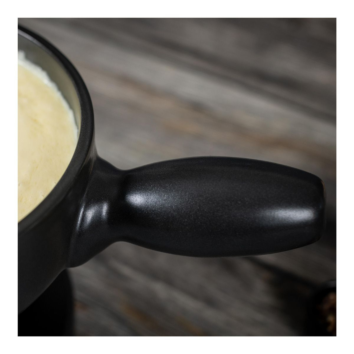 Zbliżenie czarnego uchwytu do garnka do fondue z kremowym wnętrzem na drewnianym stole.