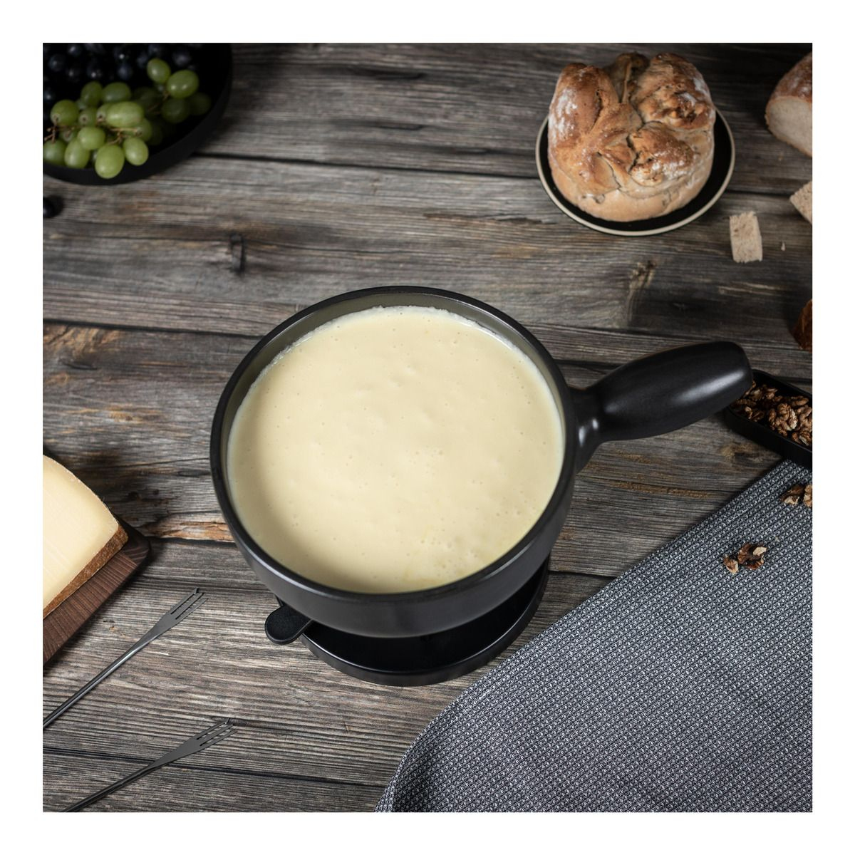 Czarny garnek do fondue z serem, chlebem, winogronami, orzechami włoskimi na drewnianym stole.