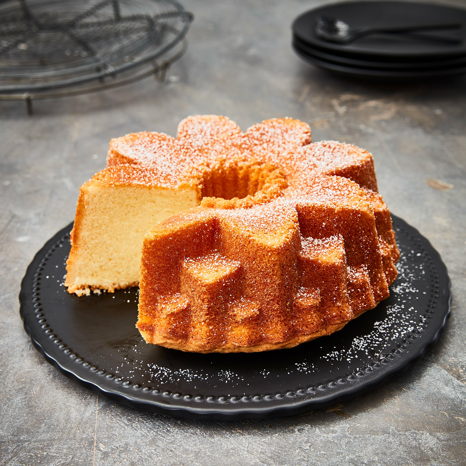 Ein Kuchen mit Loch in der Mitte, auf einem schwarzen Teller, mit Puderzucker.