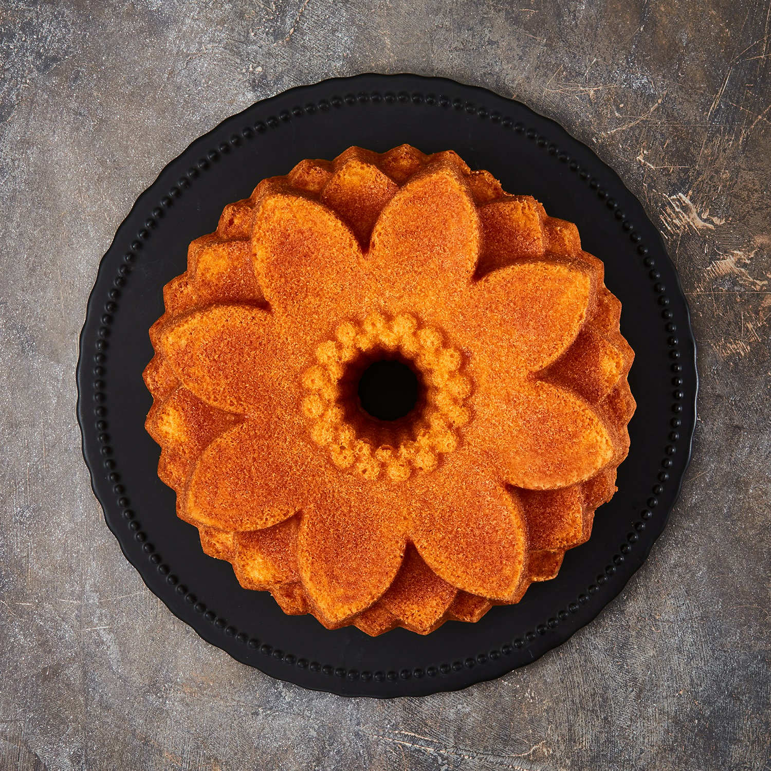 Ein blumenförmiger Kuchen auf einem schwarzen Teller, grauer Hintergrund.