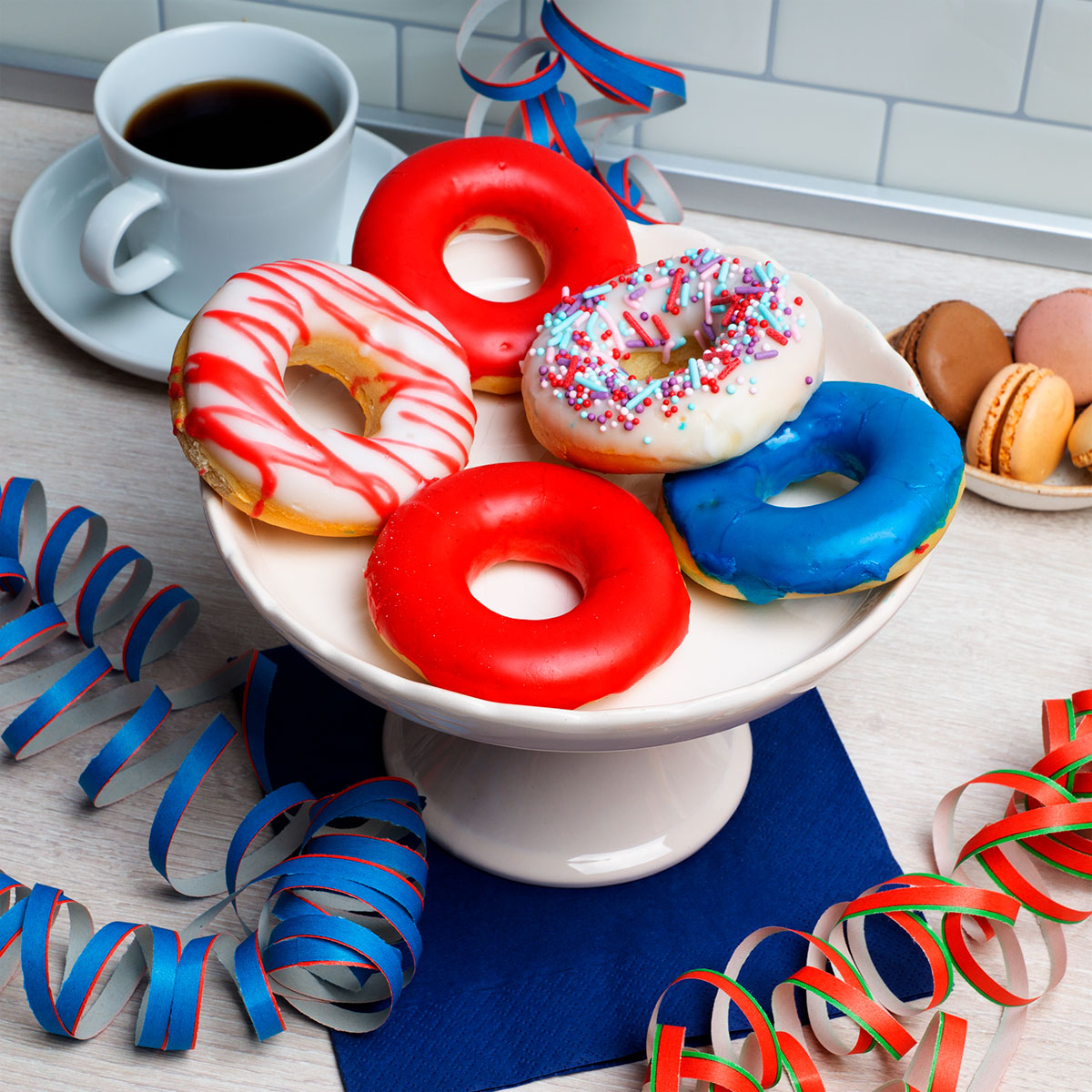 Donuts auf weißem Ständer, mit Kaffee, Makronen und Dekorationen. Bunt, festlich.