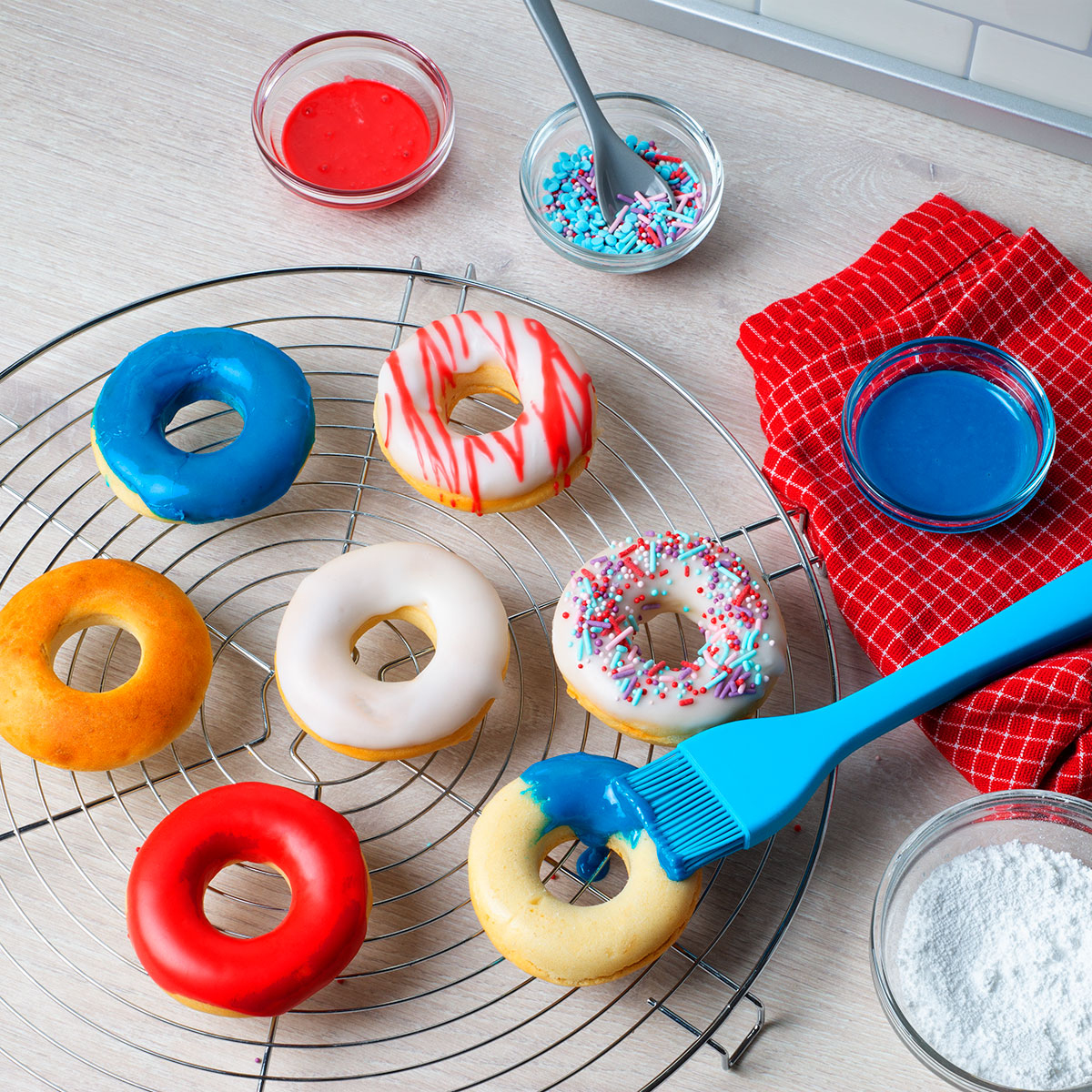 Dekorieren von Donuts mit verschiedenen Farben. Küchenumgebung mit sichtbaren Zutaten.