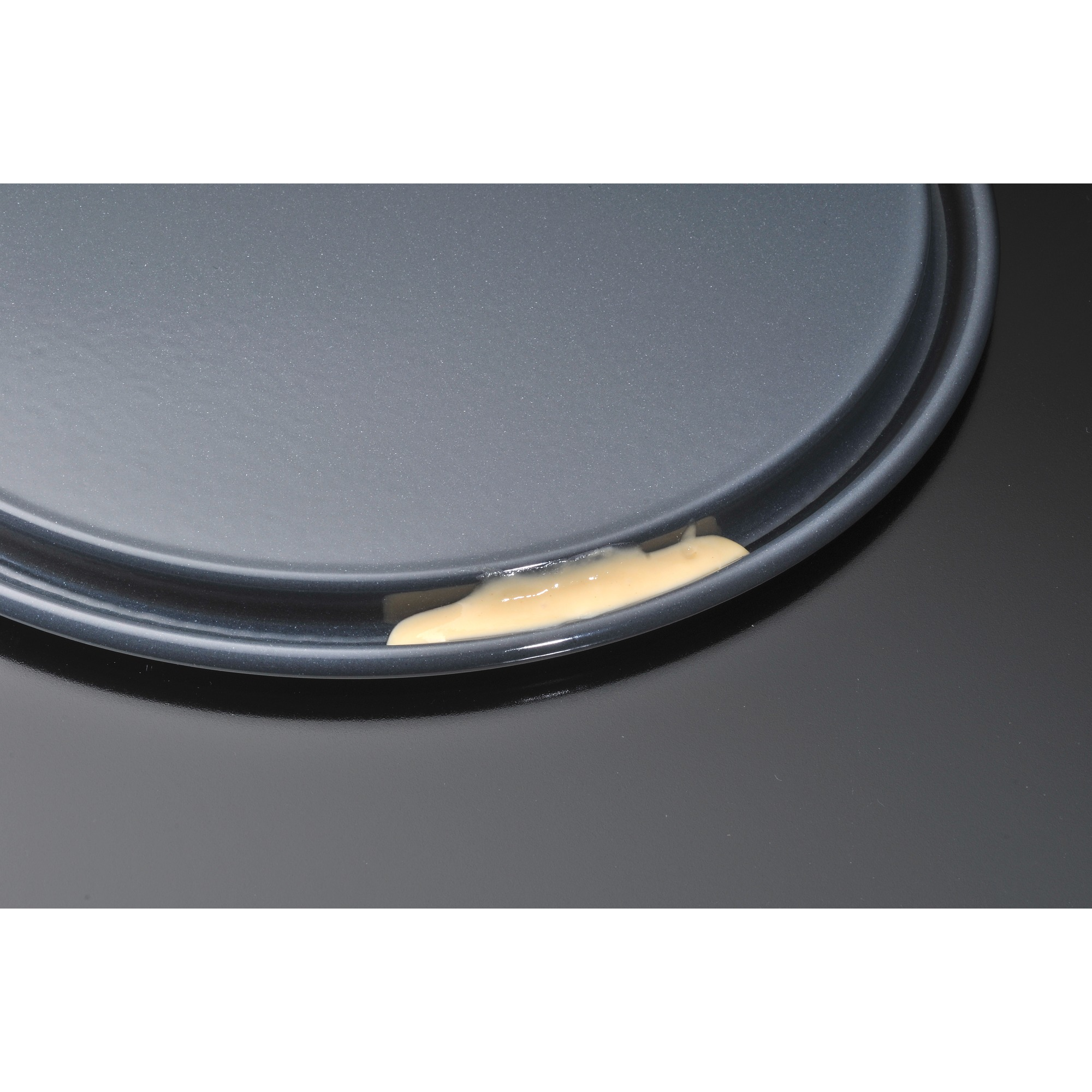 Zbliżenie ciemnoszarego talerza z małą plamą jasnej substancji na krawędzi.