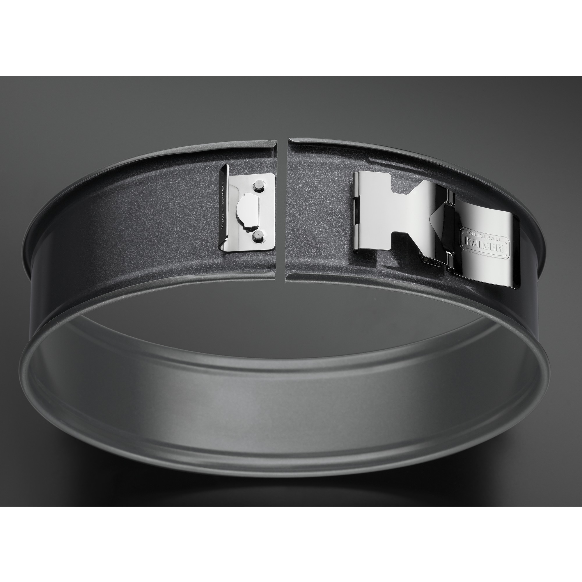 Okrągła, ciemnoszara forma do pieczenia z otwartym mechanizmem blokującym. Ciemne tło.