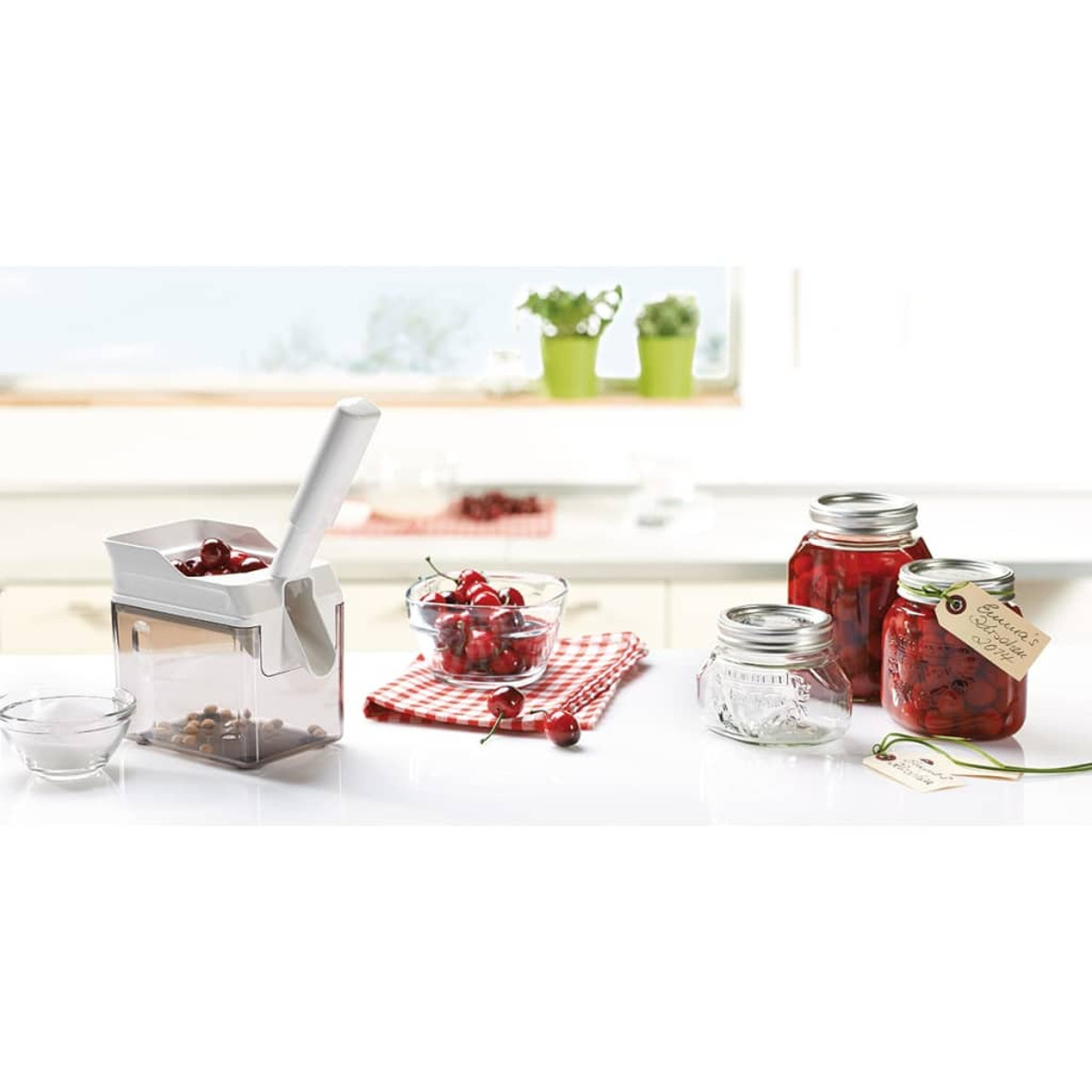 Scena kuchenna z drylownicą do wiśni, słoikami z wiśniami i małymi miseczkami z wiśniami i solą.