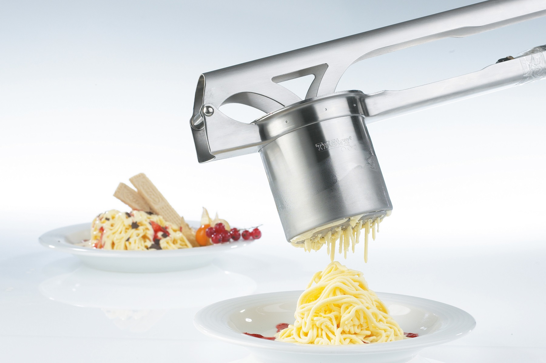 Narzędzie do robienia spaghetti. Narzędzie jest na białej powierzchni. Są dwa talerze z jedzeniem.